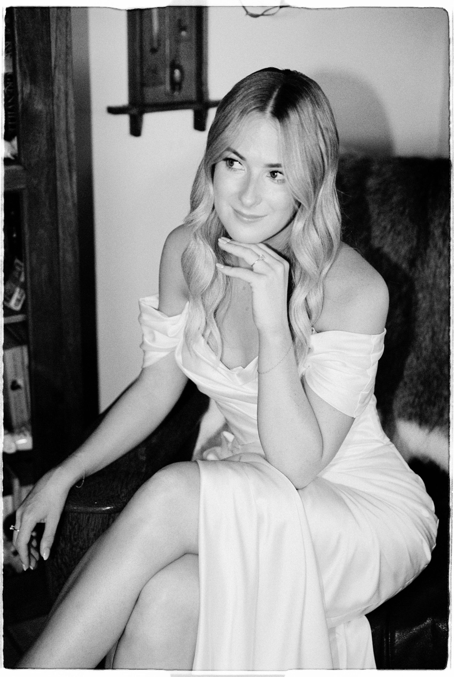 Elegant bride in off-shoulder white gown seated in black and white film photography portrait.