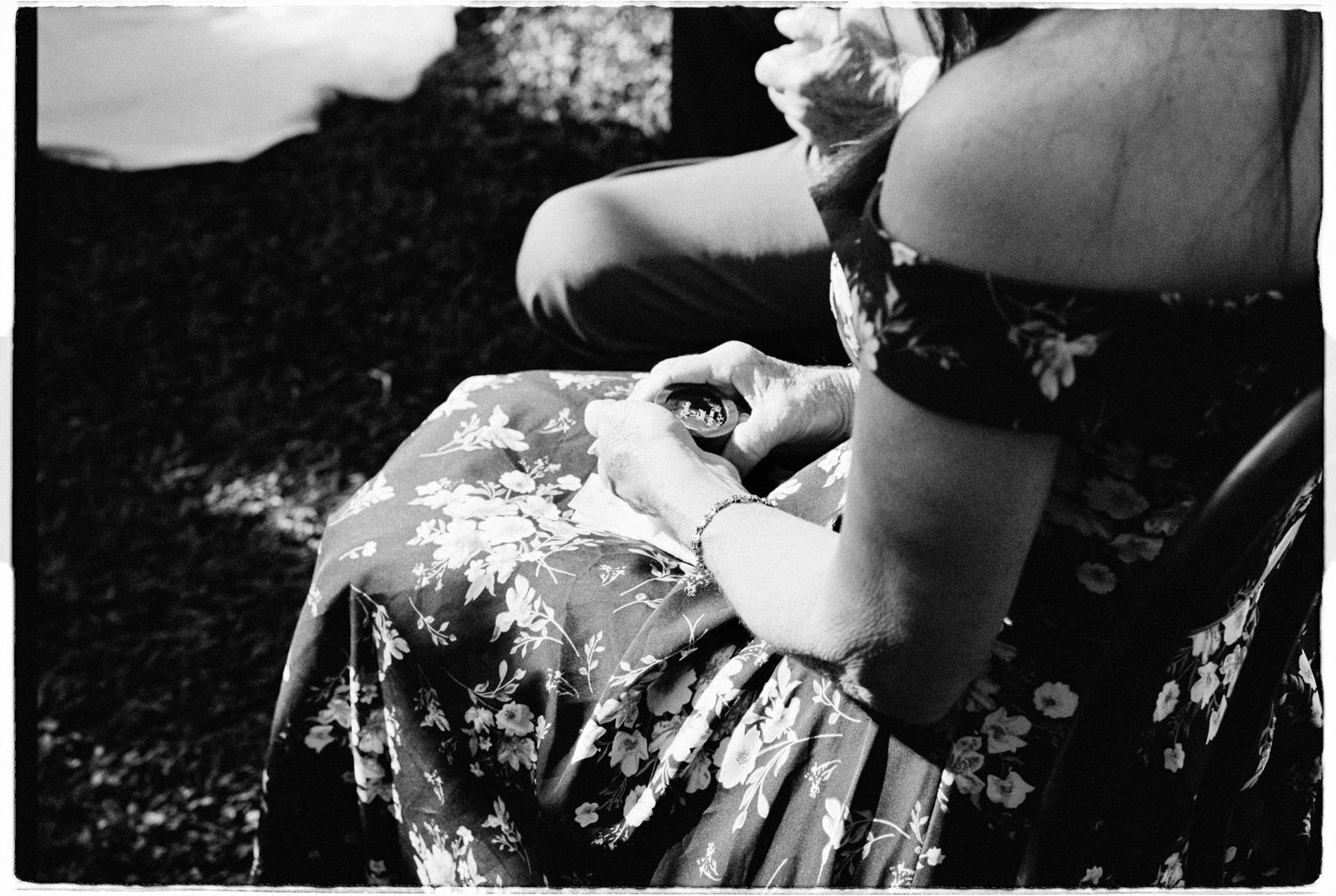 Black and white close-up of woman in floral dress adjusting bracelet outdoors.