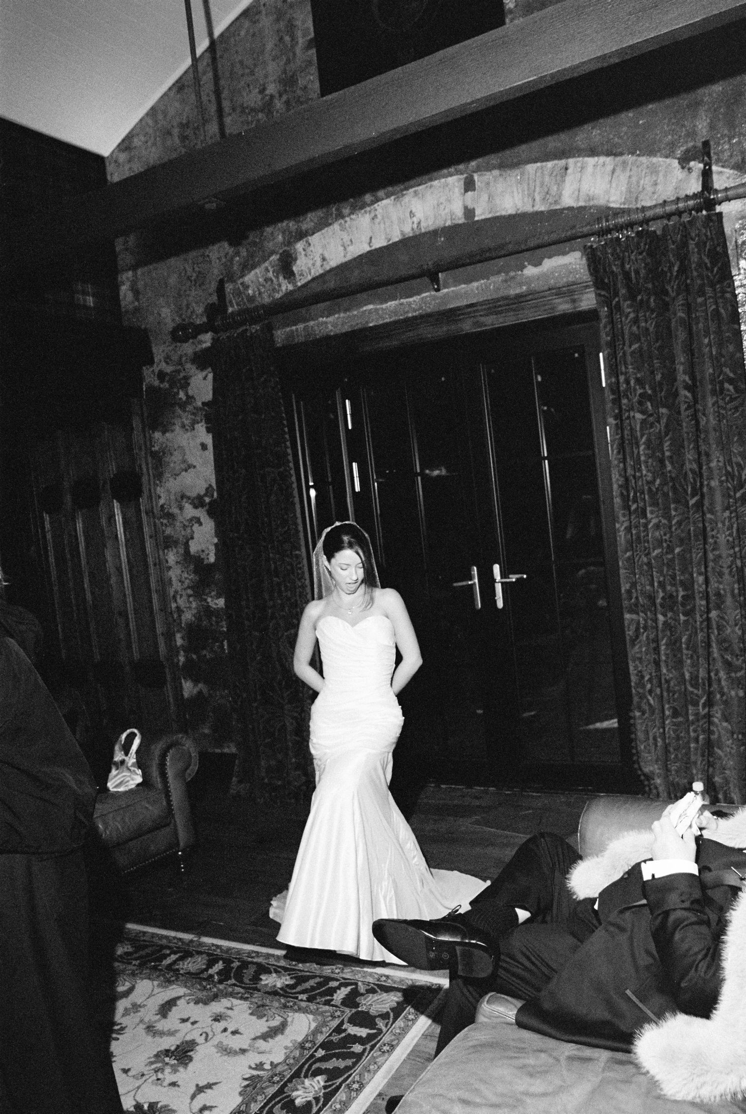 Bride in elegant mermaid wedding gown standing in dramatic doorway of rustic venue.