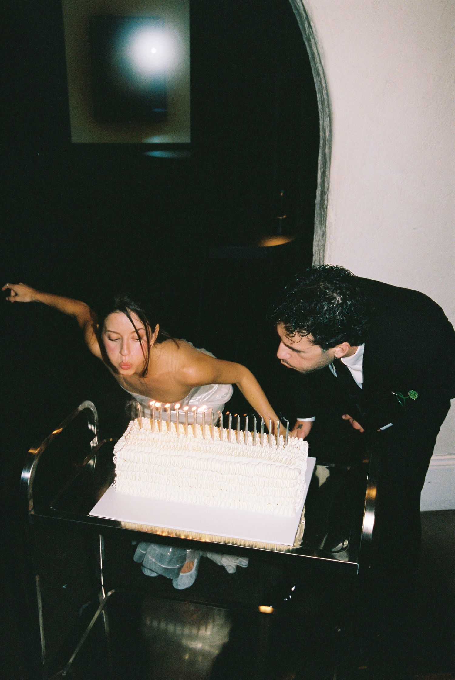 Bride and groom blowing out candles on a white wedding cake together.