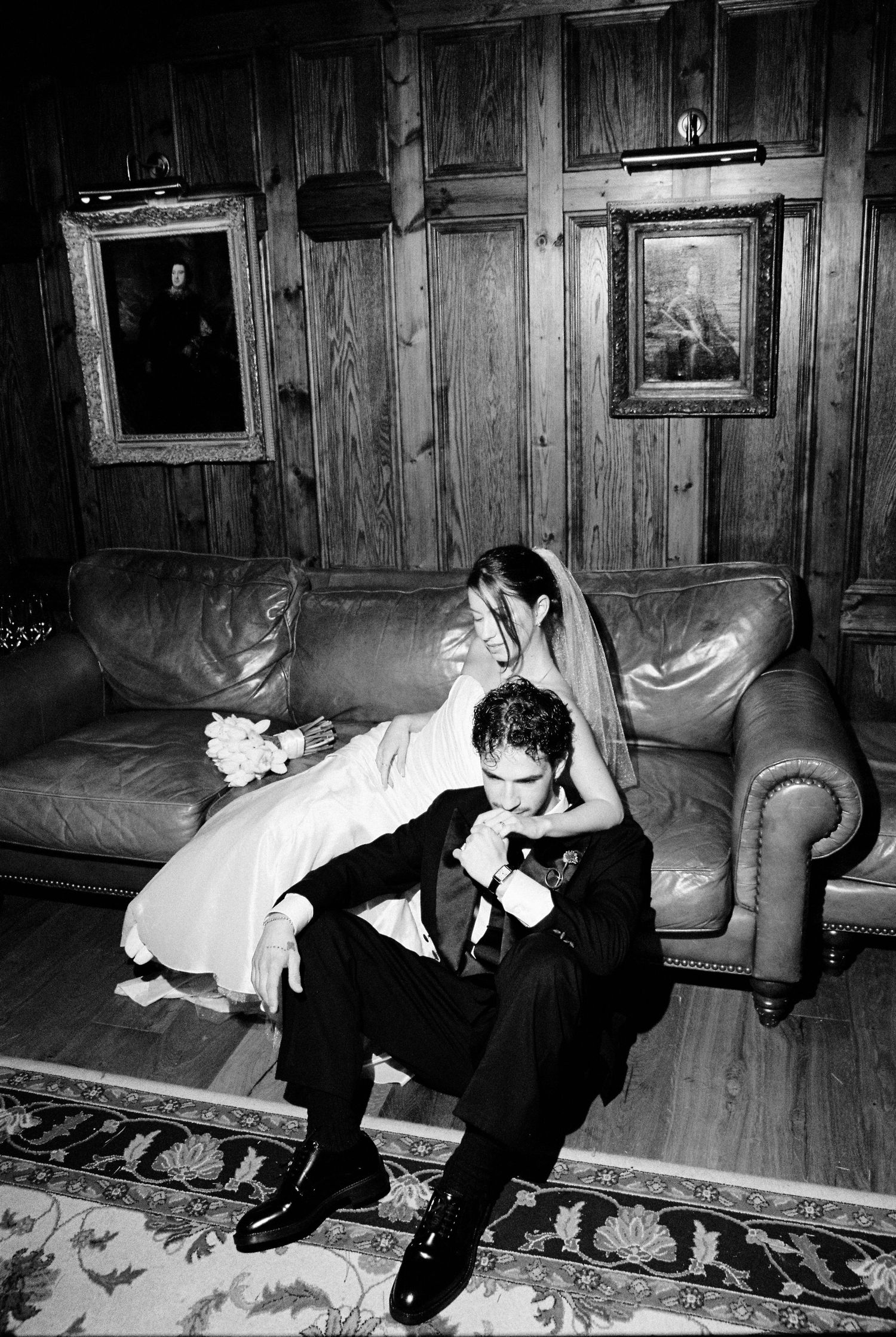 Black and white photo of bride and groom sharing intimate moment on leather sofa.