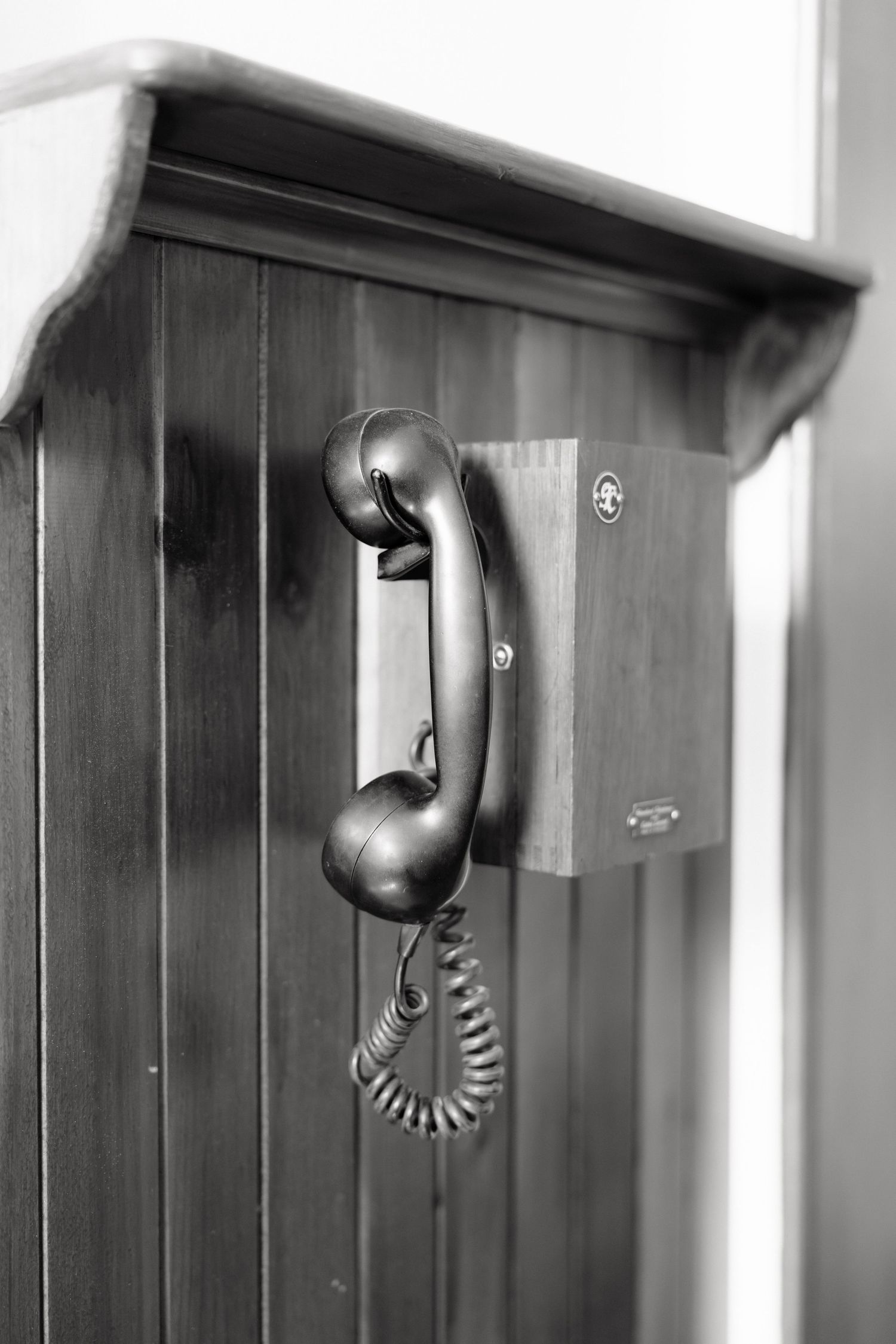 Vintage black rotary telephone handset mounted on a wooden wall panel in black and white photography.