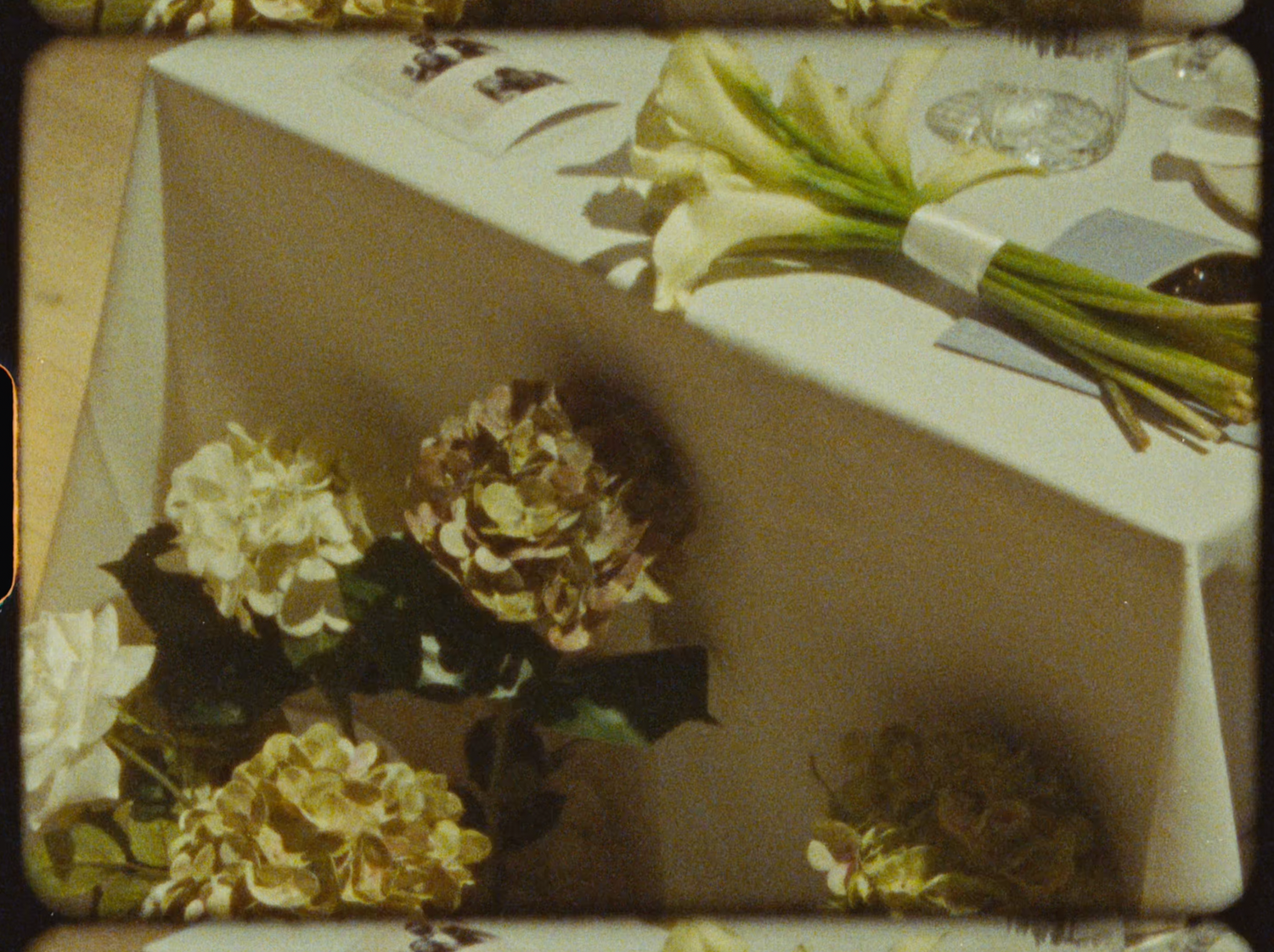 Wedding table centerpiece featuring white hydrangeas and calla lilies on a white tablecloth.