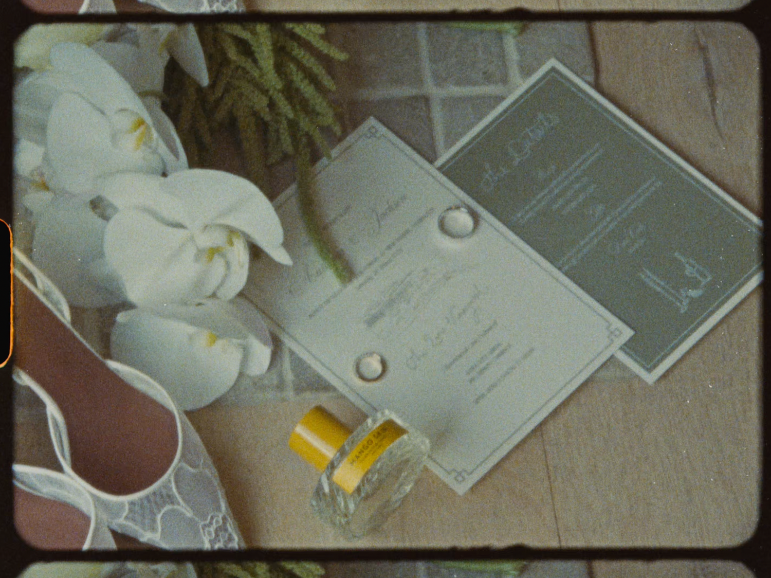 Wedding flat lay with lace shoes, white orchids, gold rings, perfume, and elegant invitations.