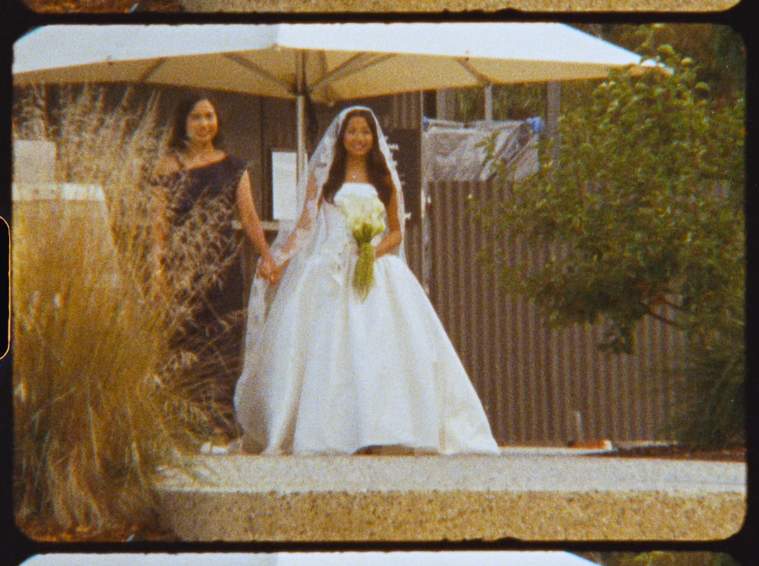 Bride in white ball gown holding bouquet walking with escort at outdoor vineyard wedding.