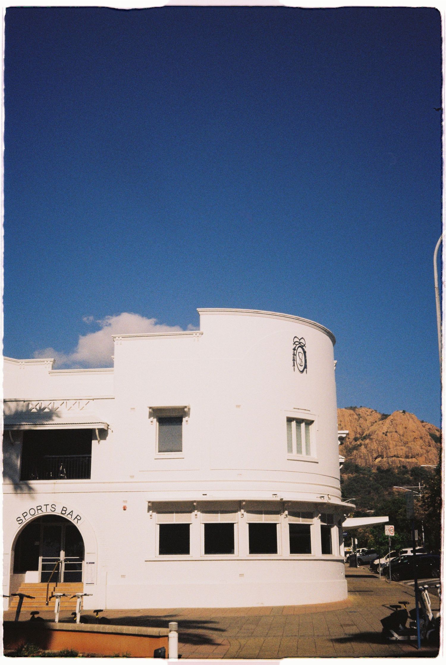 White Art Deco sports bar building with curved facade against vivid blue sky and rocky hill.