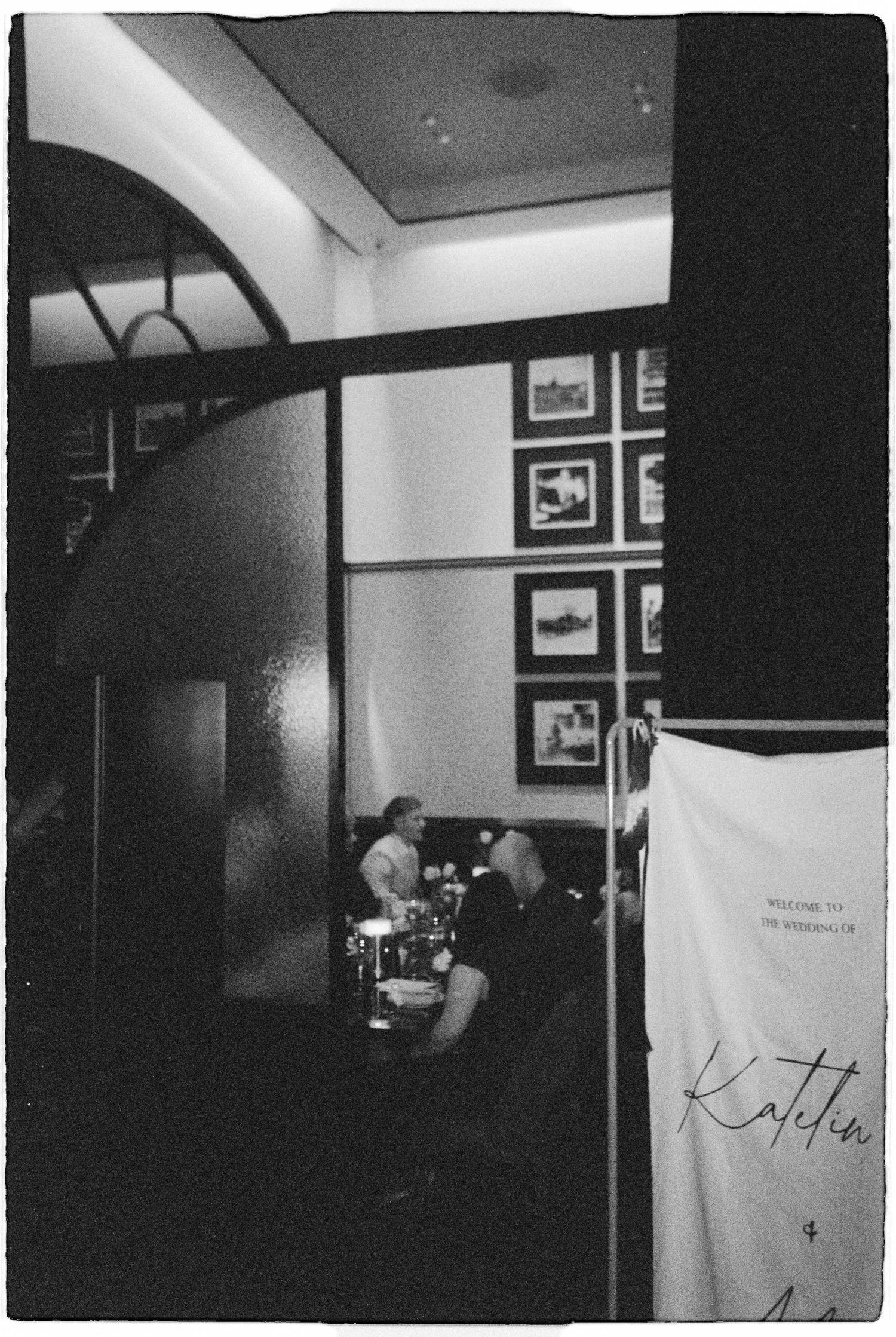 Black and white film photo of wedding reception interior with welcome sign bearing couple names.