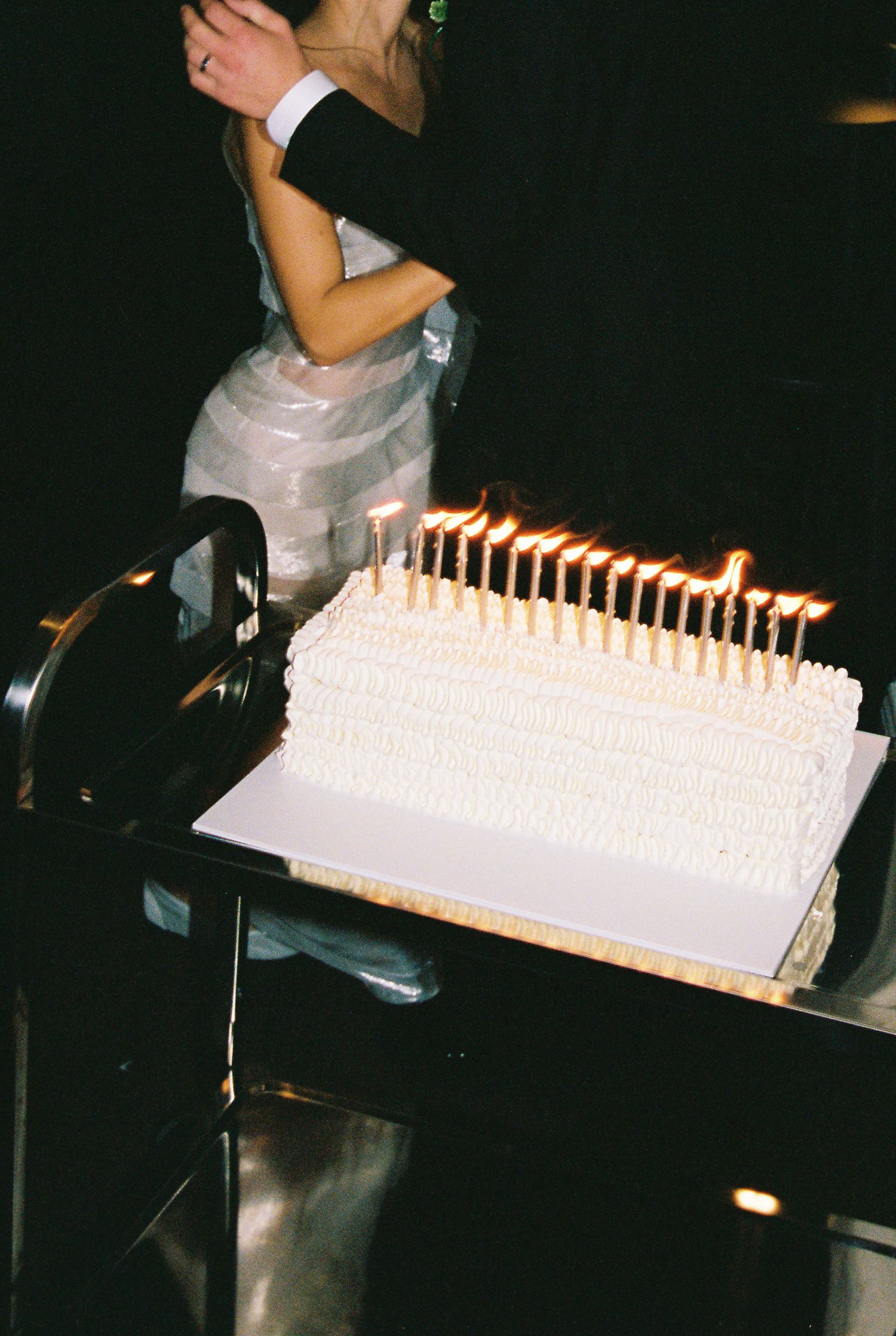 Close-up of a white wedding cake with rows of lit candles at a formal reception.