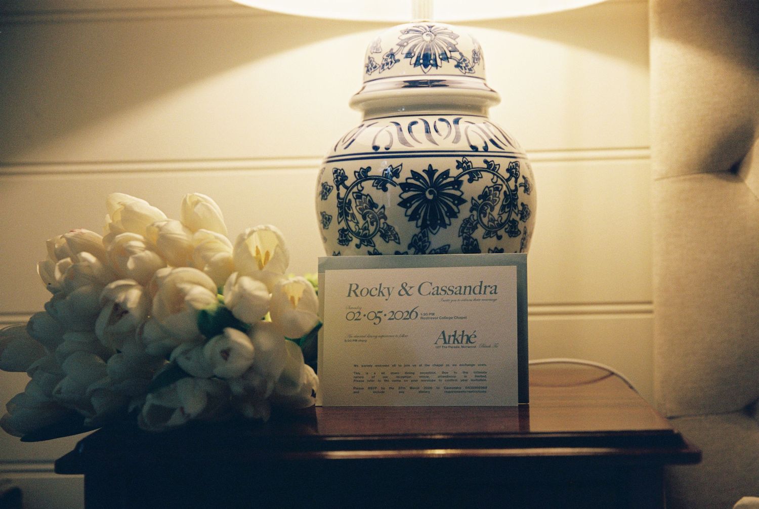 Wedding name card for Rocky and Cassandra beside white tulips and a blue and white ceramic lamp.