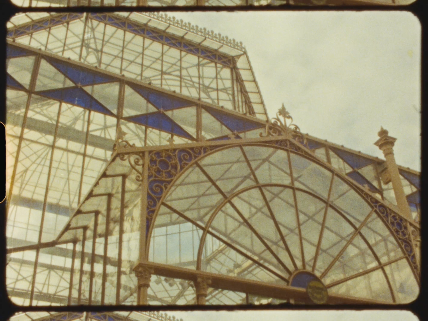 Ornate Victorian greenhouse with blue geometric glass panels and decorative ironwork against a bright sky.