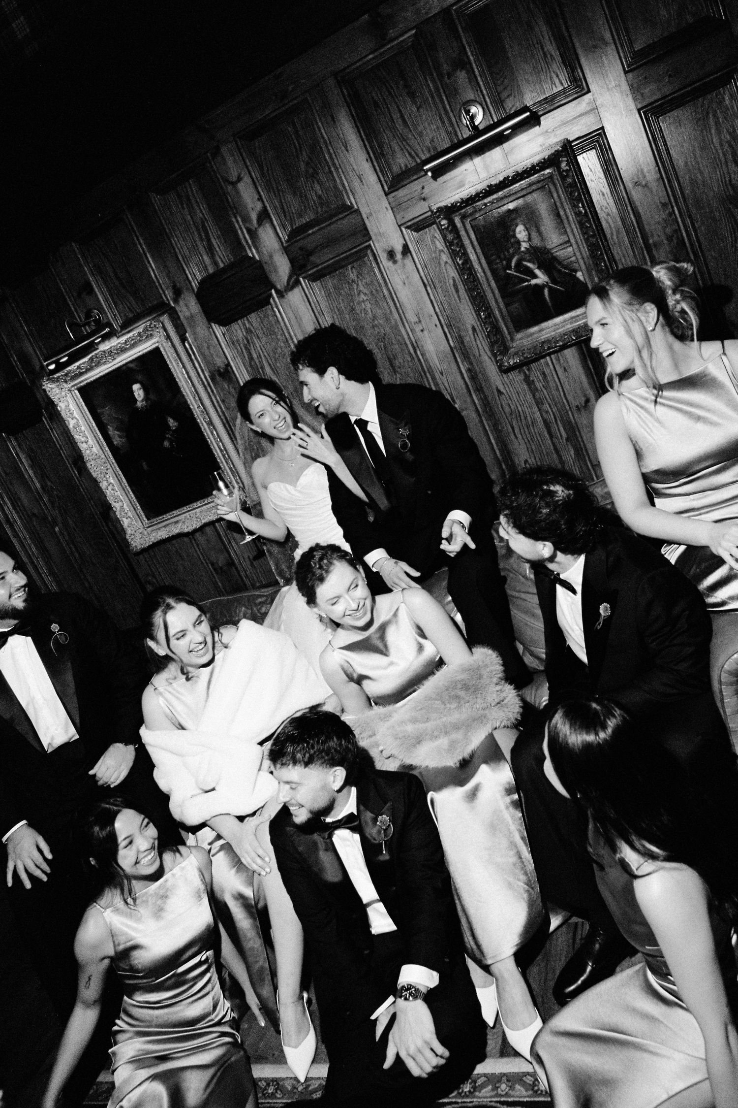 Wedding guests dance and celebrate joyfully in wood-paneled ballroom adorned with portrait paintings.