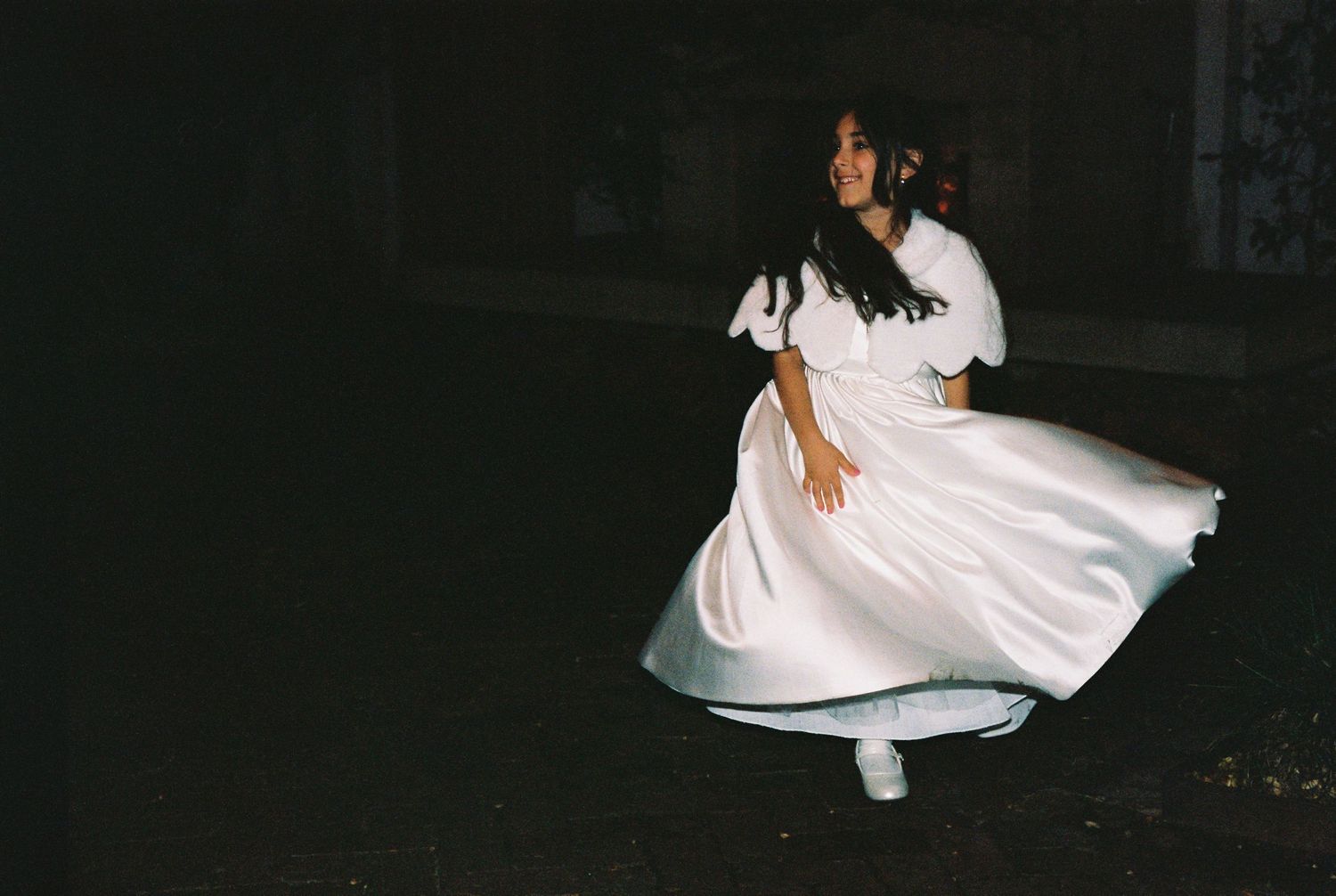 Bride in white satin dress twirling dramatically in a dark outdoor setting at night.