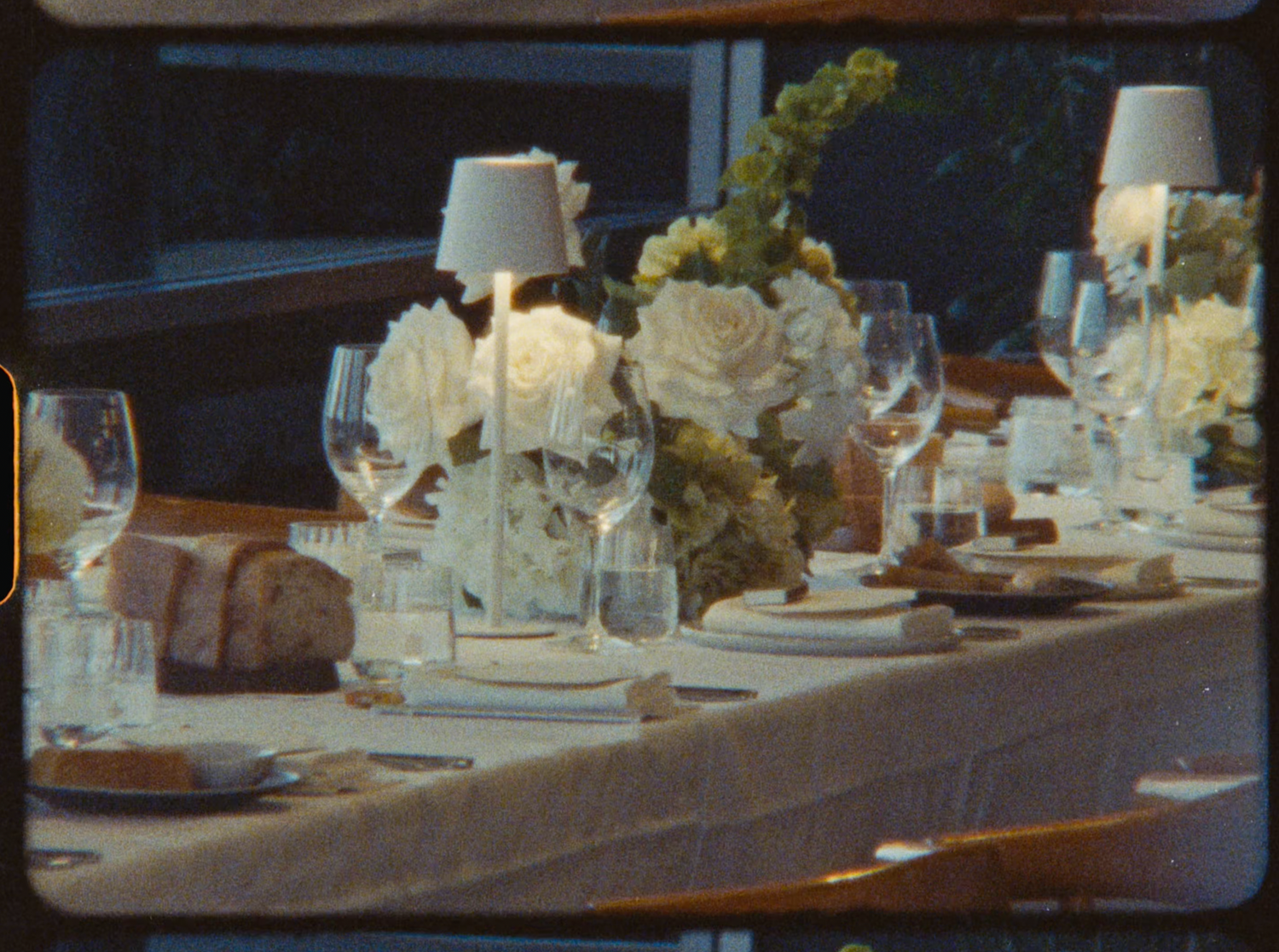 Elegant wedding reception table set with white roses, crystal glasses, and candle centerpieces.