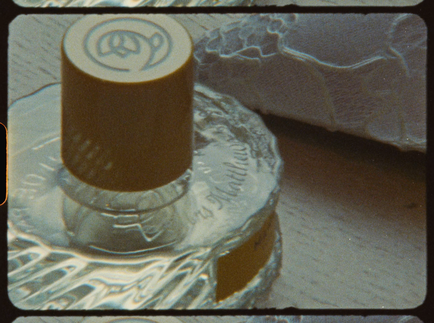 Close-up of a glass perfume bottle with a gold cap on a reflective silver surface.