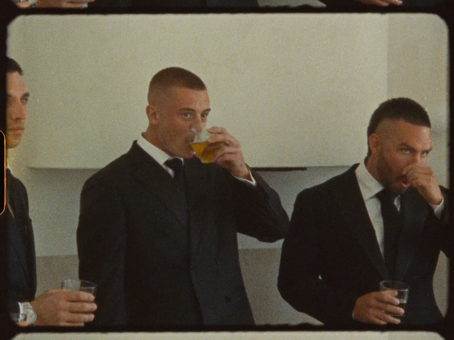 Groomsmen in black suits drinking beer together during pre-wedding celebrations indoors.