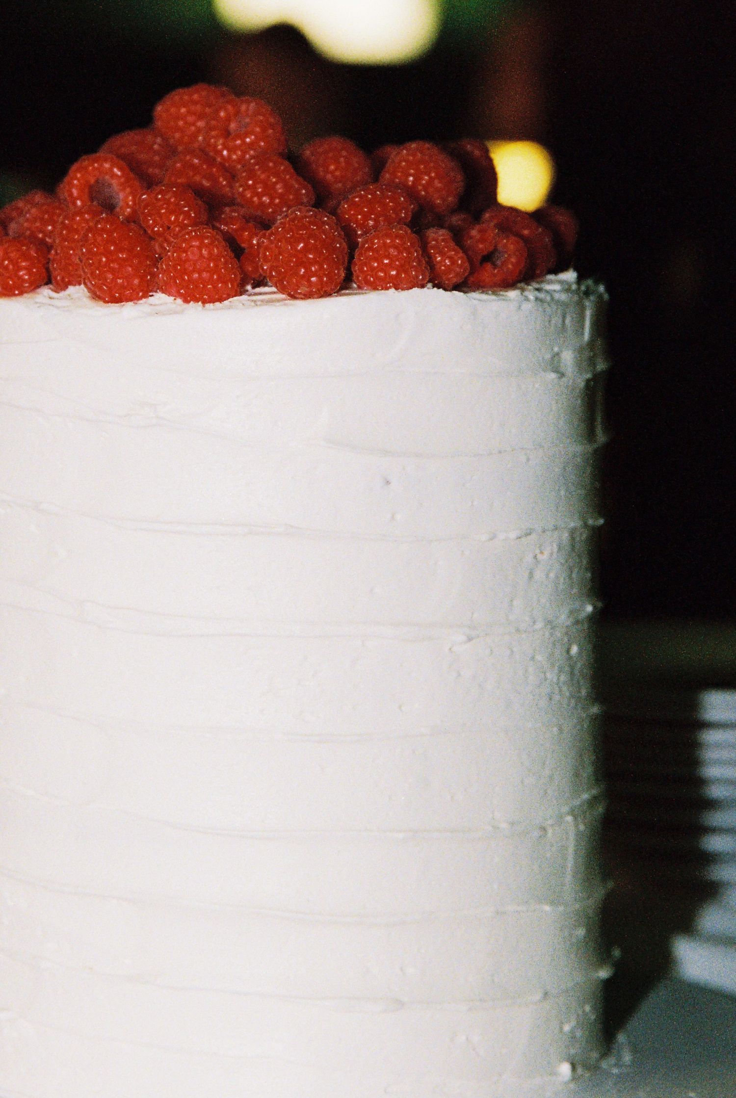 Elegant white textured wedding cake topped with fresh red raspberries on a dark background.