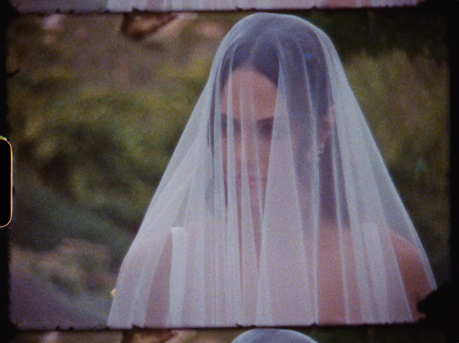 Bride wearing a delicate white wedding veil covering her face, standing outdoors in a romantic, ethereal bridal portrait.