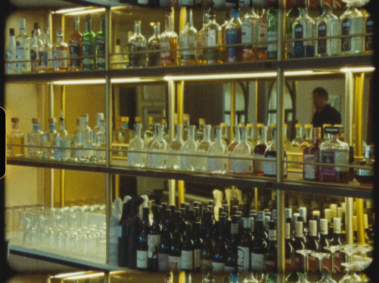 Well-stocked bar shelves displaying various liquor bottles and glassware with warm golden lighting.