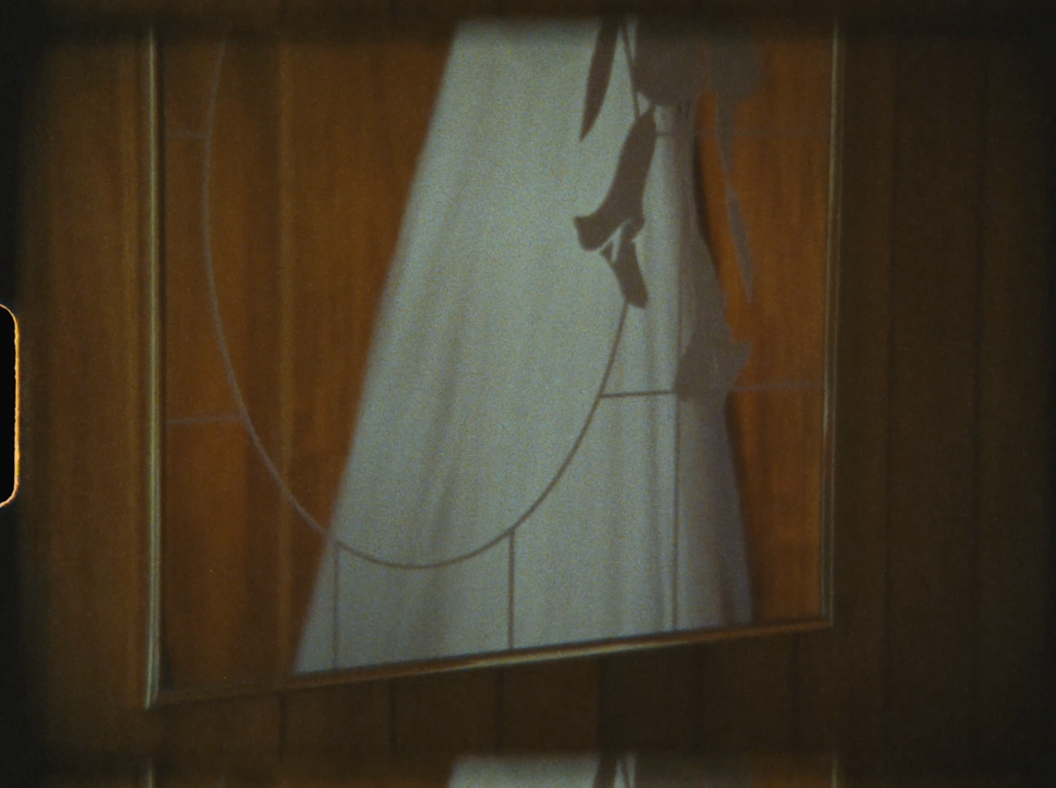 A white curtain partially drawn back on a wooden curtain rod, framed by dark brown wooden panels.