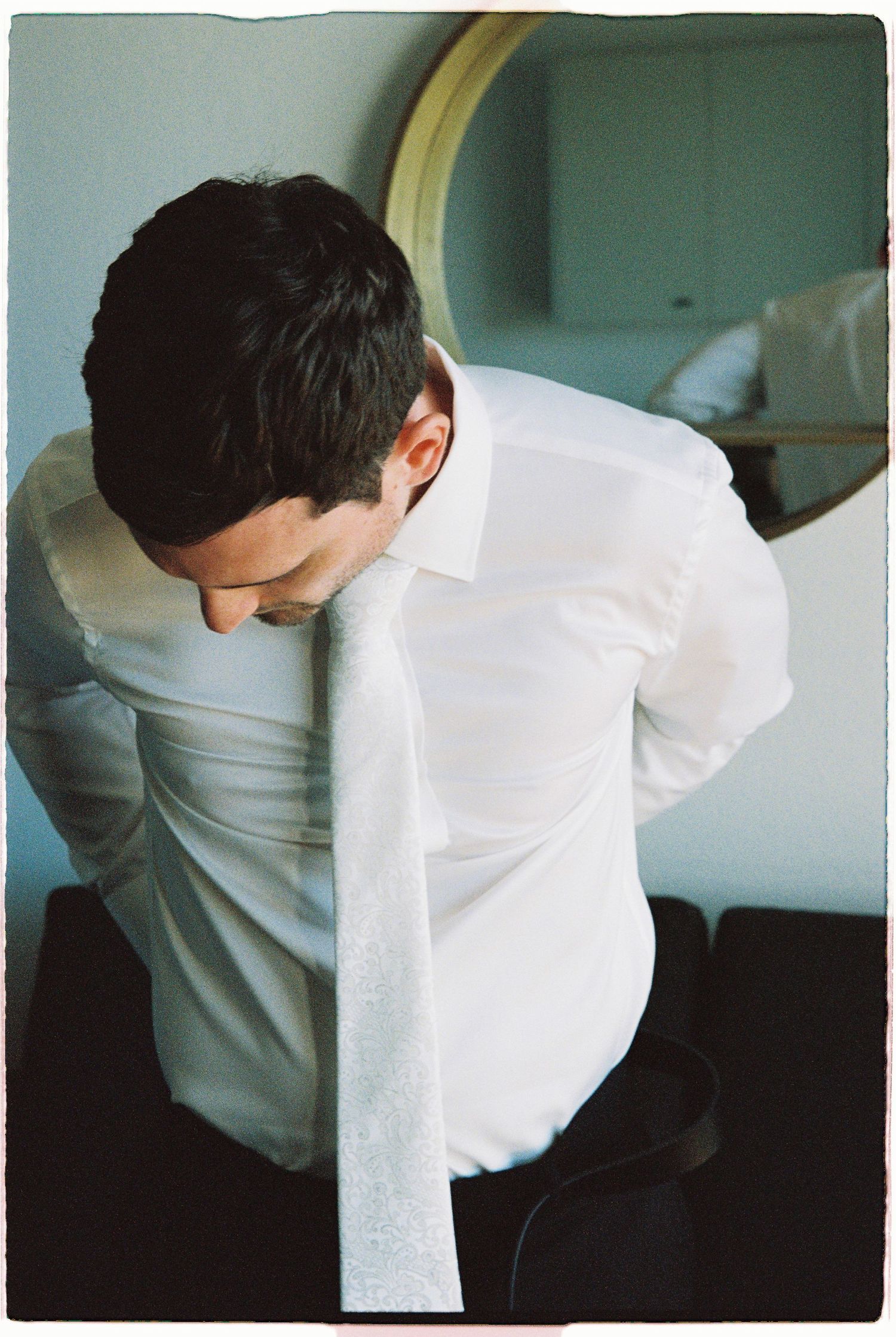 Groom in white dress shirt adjusting his tie while getting ready for his wedding day.
