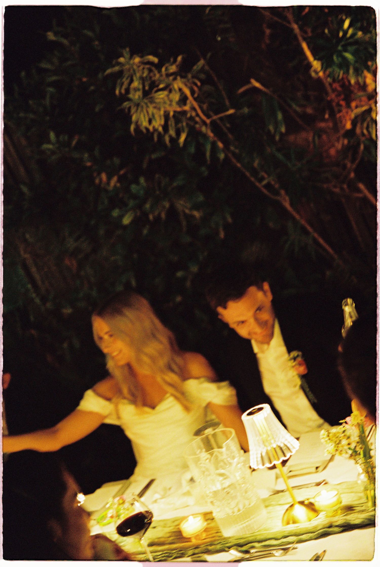 A bride and groom share a romantic moment at a candlelit outdoor wedding reception dinner table.