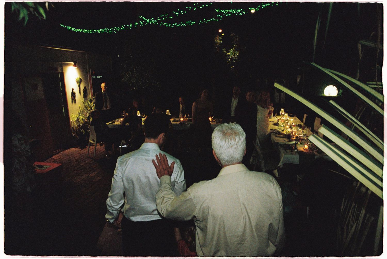 Guests mingle at a warmly lit outdoor wedding reception venue at night.
