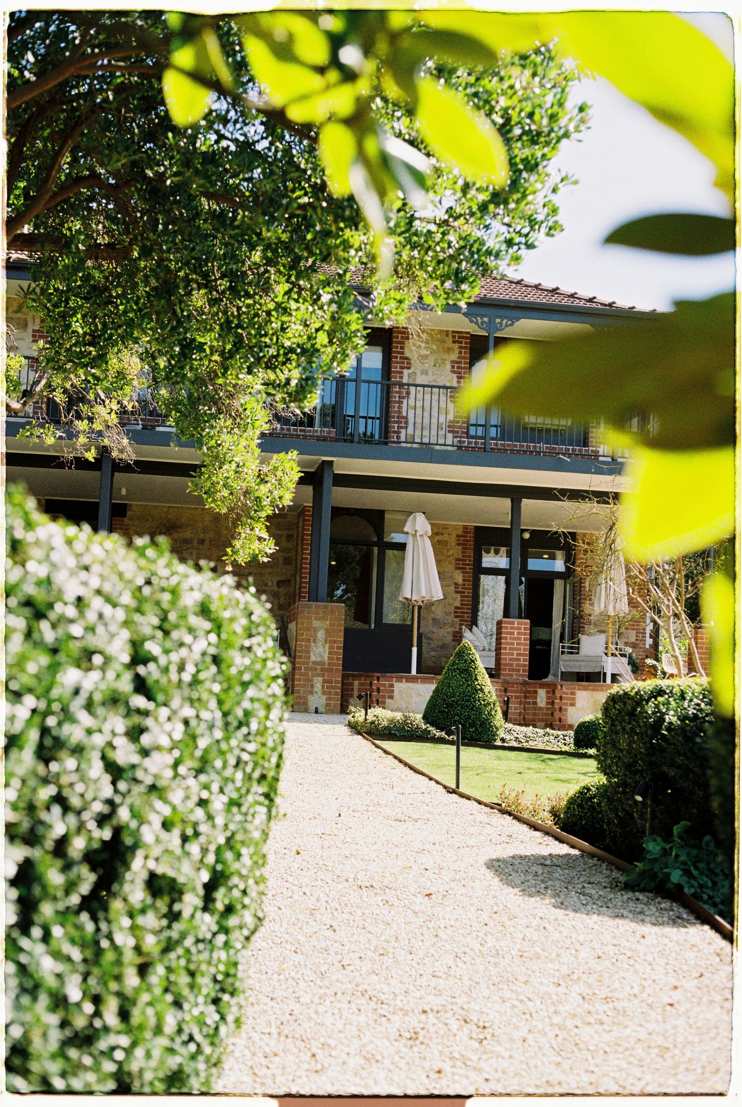 Charming brick wedding venue with manicured gardens and gravel pathway on a sunny day.