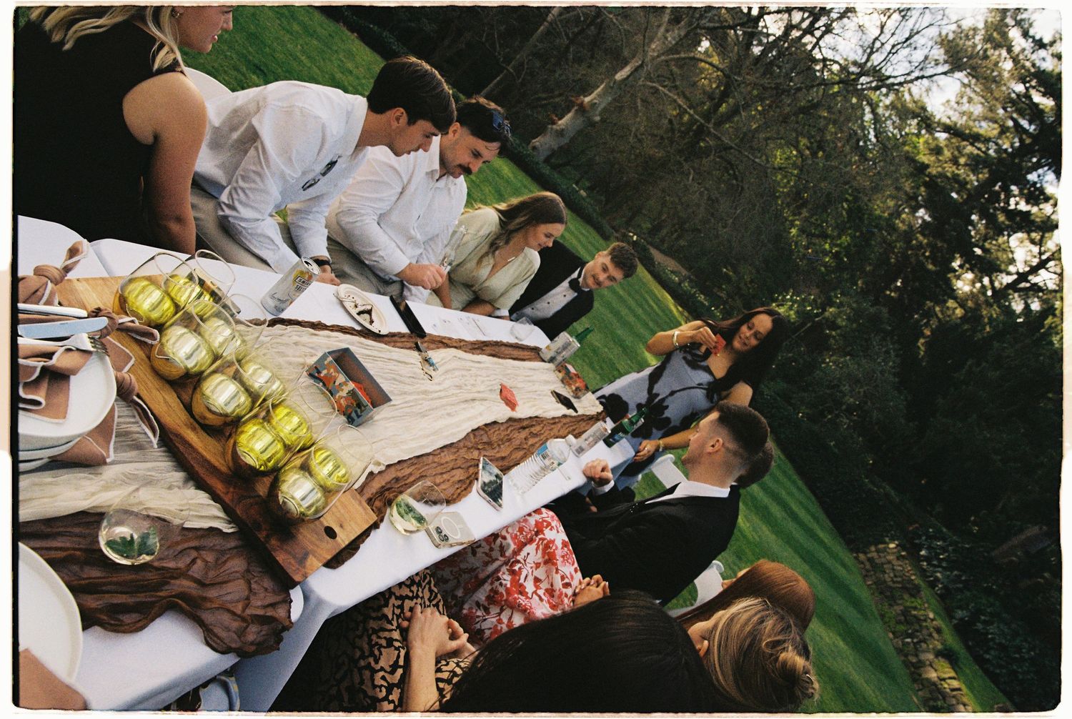 Guests gathered around an outdoor wedding reception table with decorative green apples and rustic wooden decor.