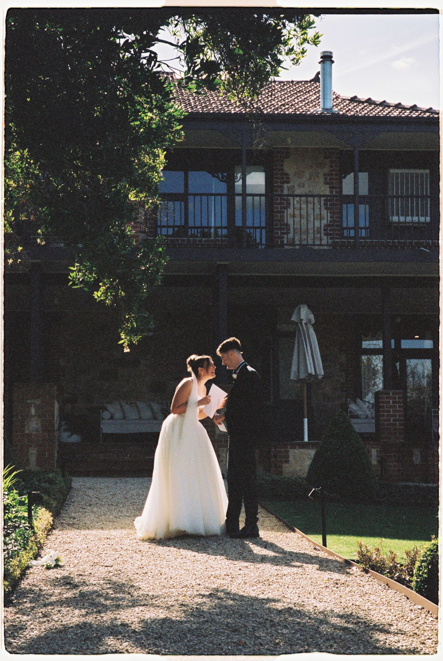 Bride and groom standing together on gravel path outside rustic stone wedding venue.