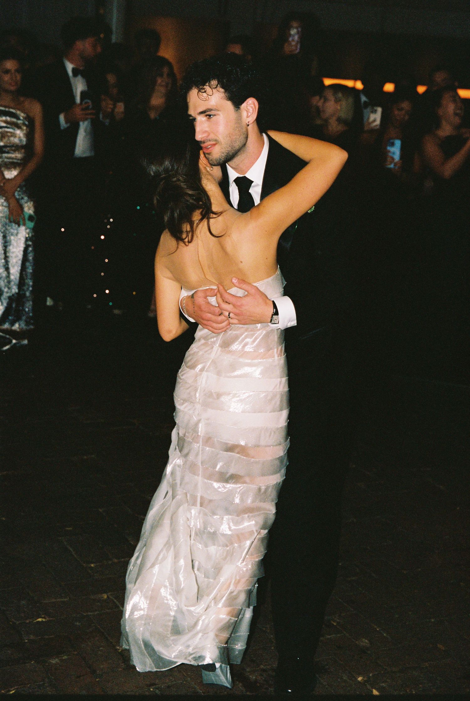 Couple sharing first dance at wedding reception, bride in backless tiered white gown, groom in black suit.