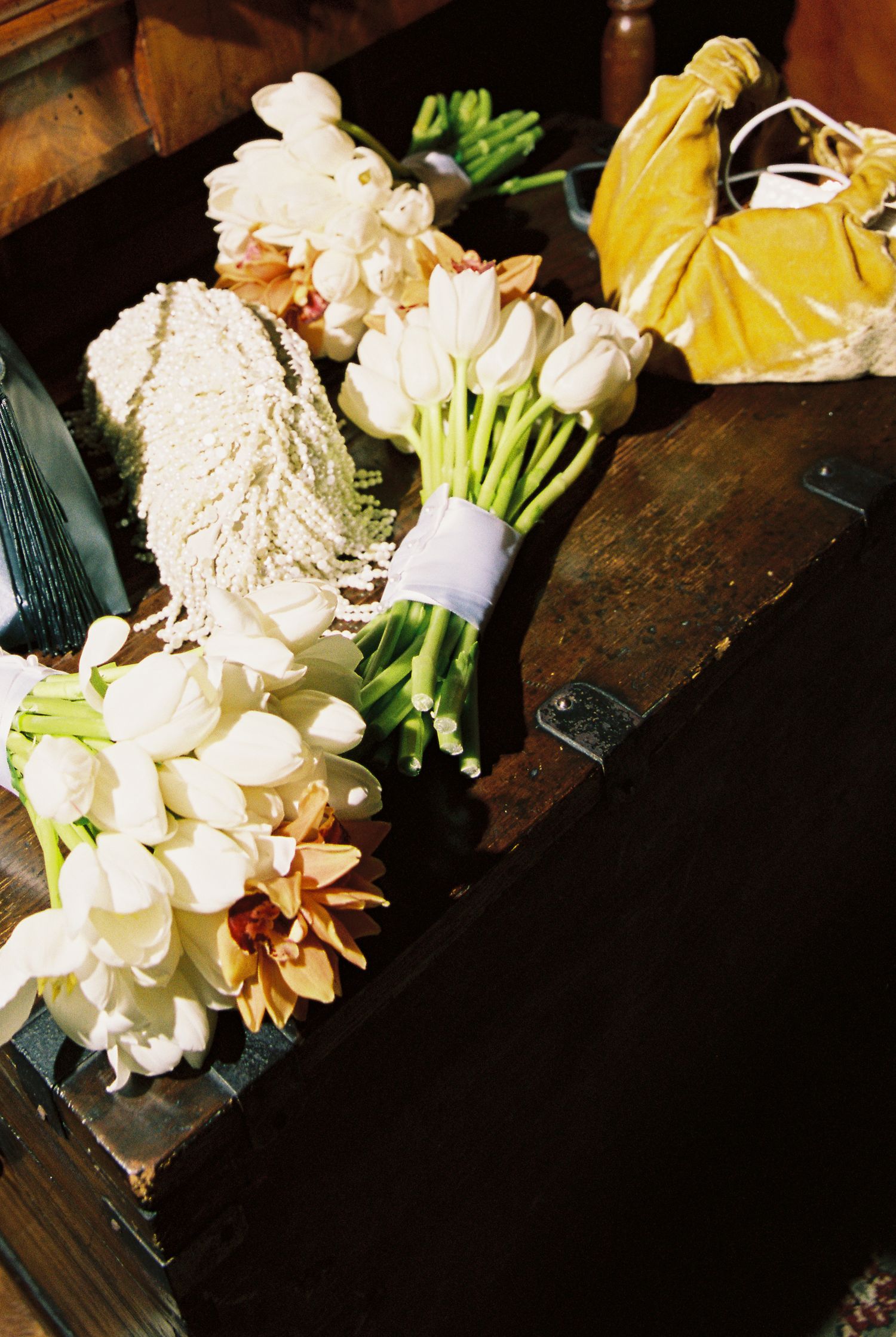 White tulip and orchid wedding bouquets arranged on dark wooden surface with yellow bag.