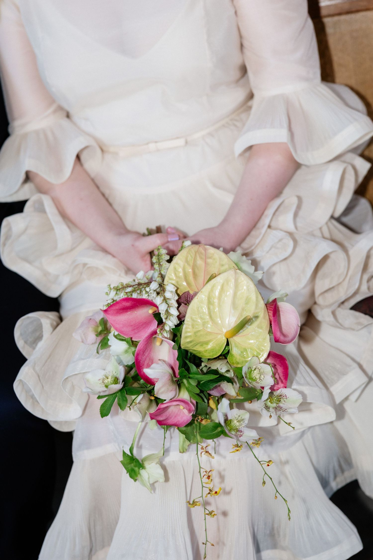 Bride in ruffled white dress holding pink and green anthurium wedding bouquet with cascading flowers.