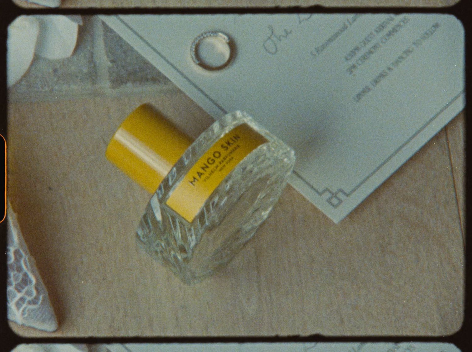 Mango Skin perfume bottle with yellow cap resting on wedding stationery and invitation suite.