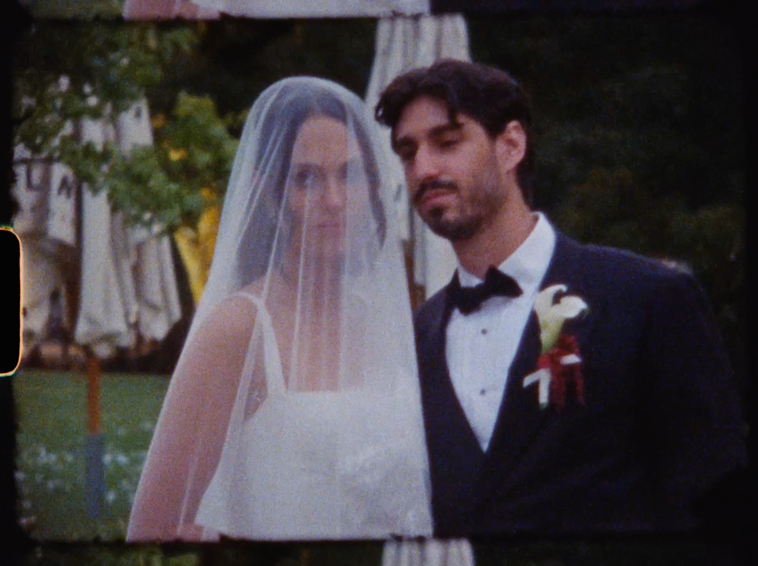 Close-up of bride in white gown with veil and groom in black tuxedo with boutonniere at wedding.