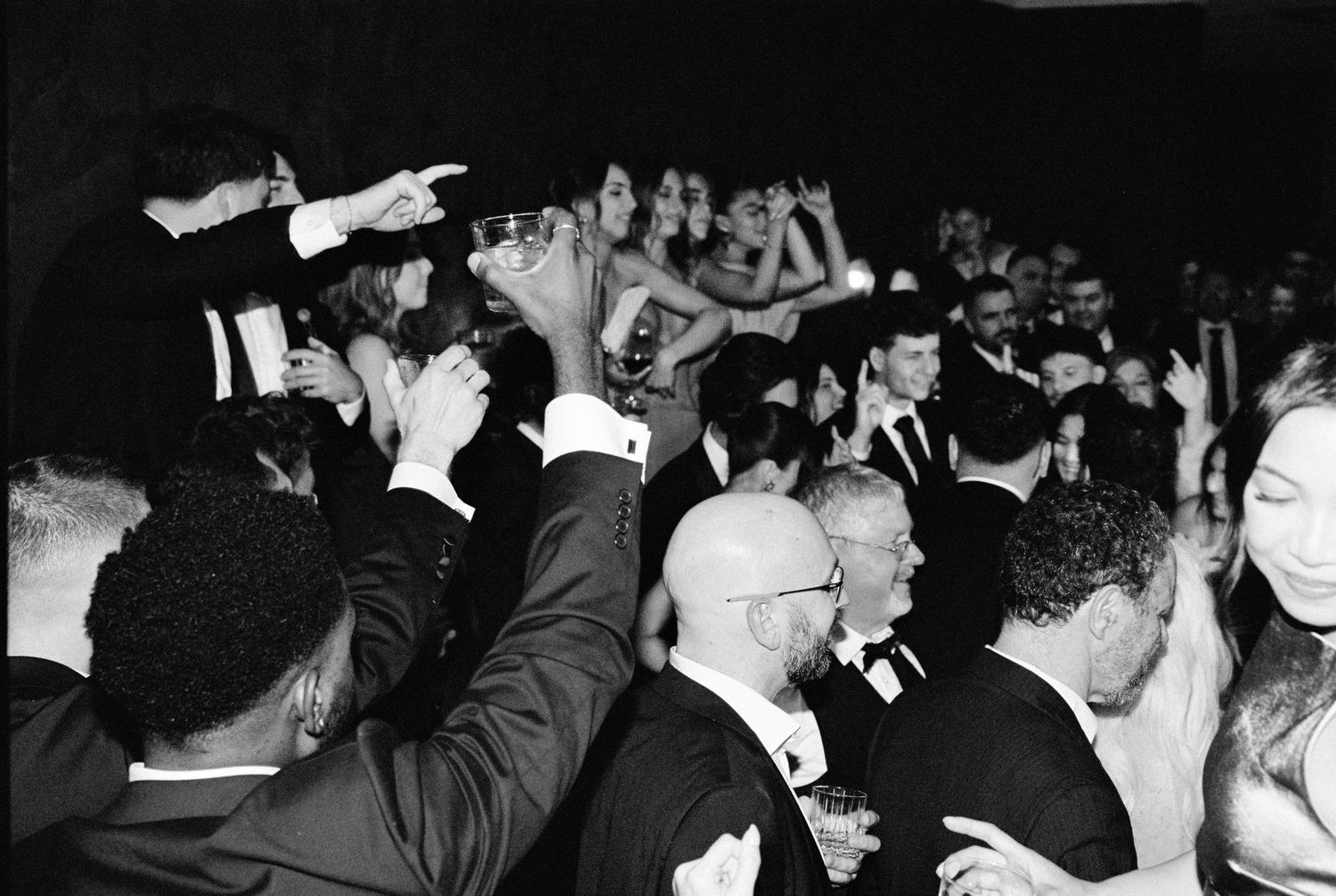 Energetic wedding reception dance floor packed with guests in formal black tie attire.