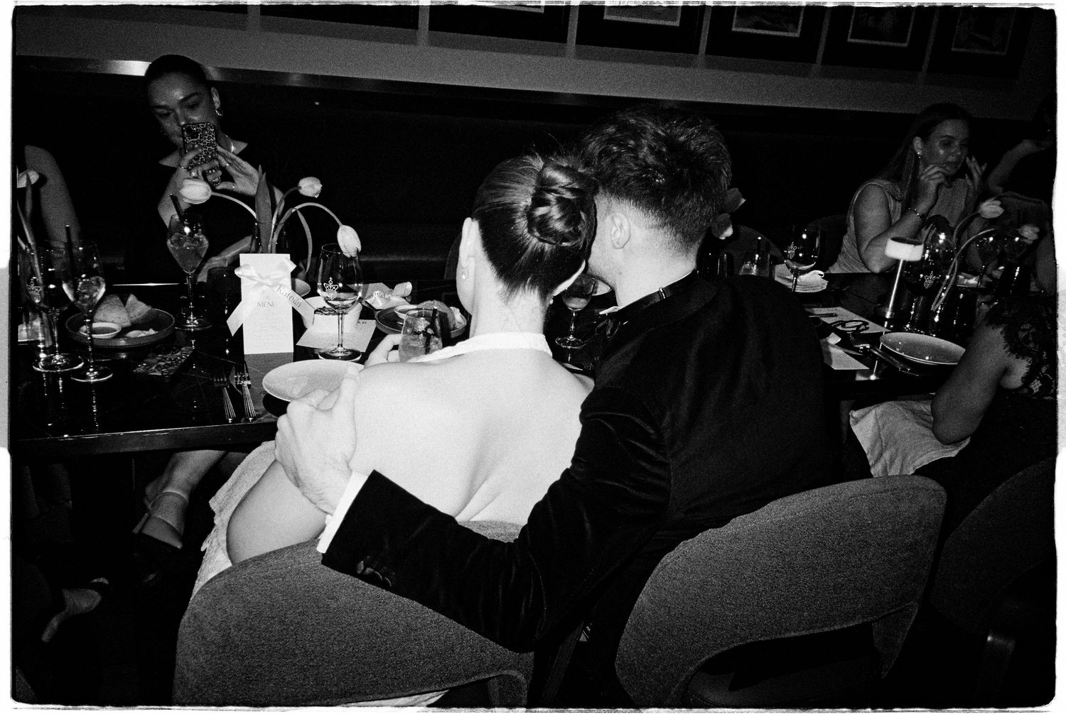 Black and white photo of elegantly dressed couple dining at upscale restaurant, woman in backless dress.