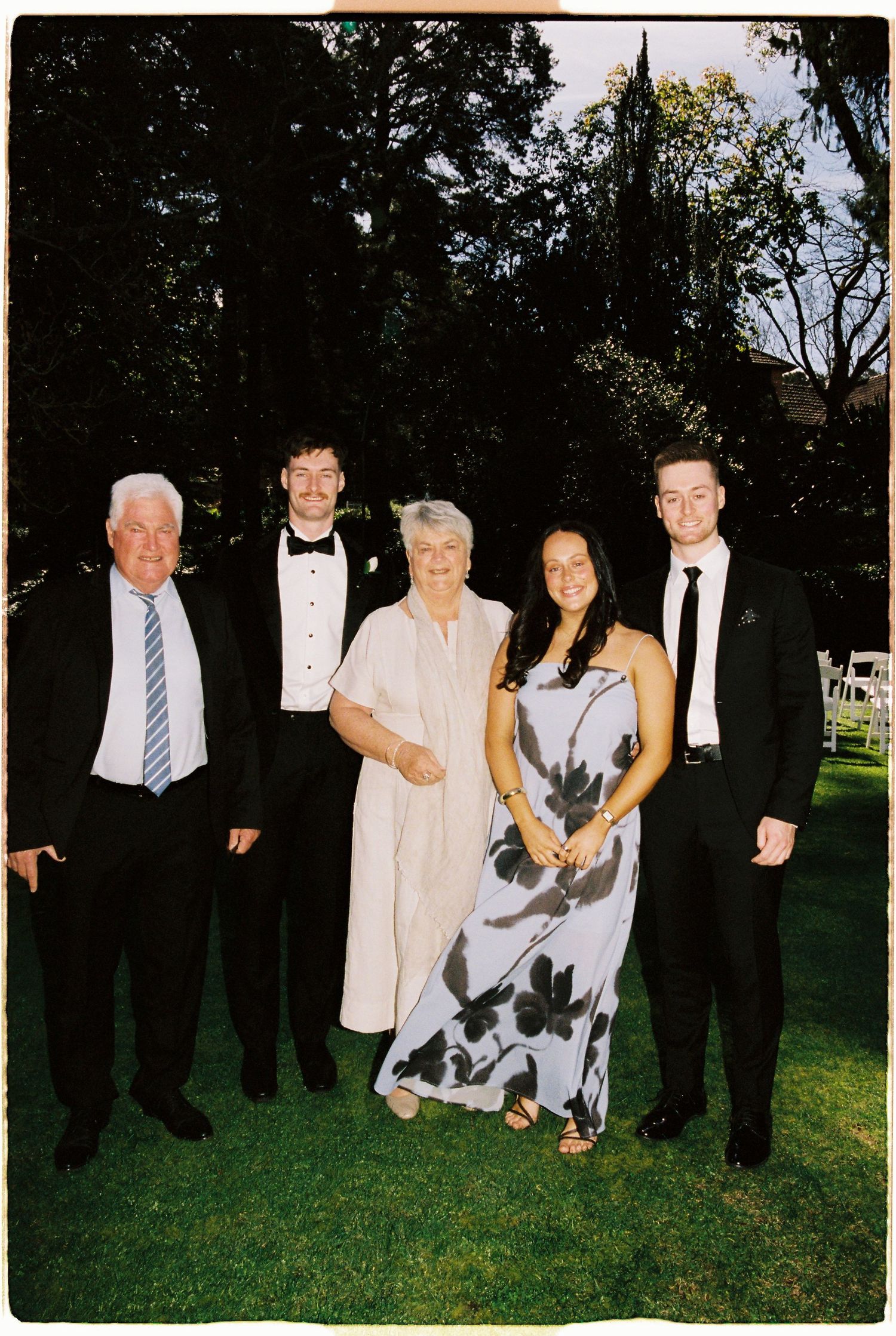 Family of five poses together on green lawn at outdoor wedding celebration.