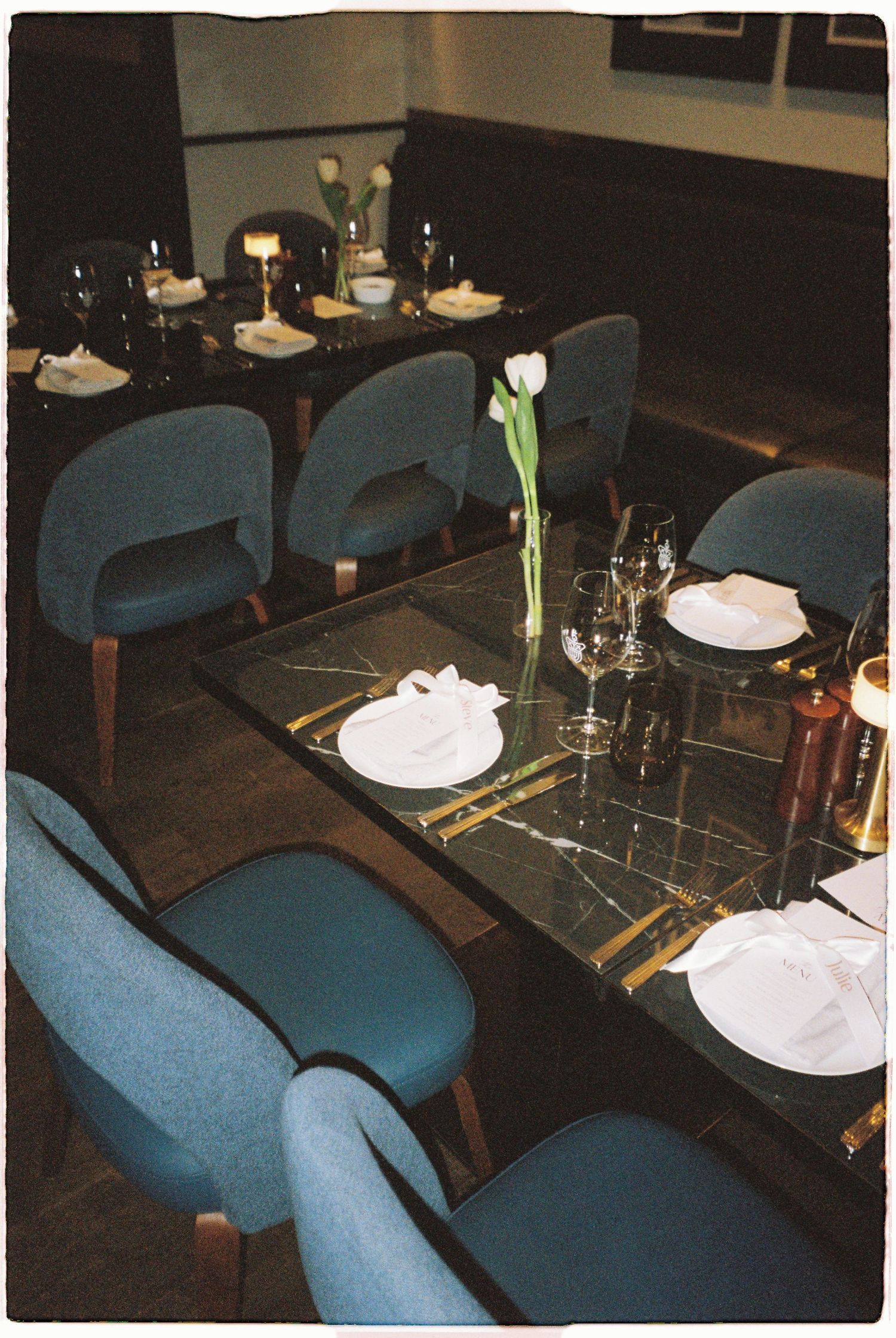 Elegant restaurant tables set with white tulips, wine glasses, and folded napkins for a wedding dinner.
