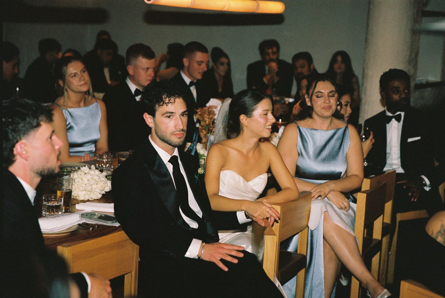 Wedding guests seated at reception tables watching a speech or presentation.