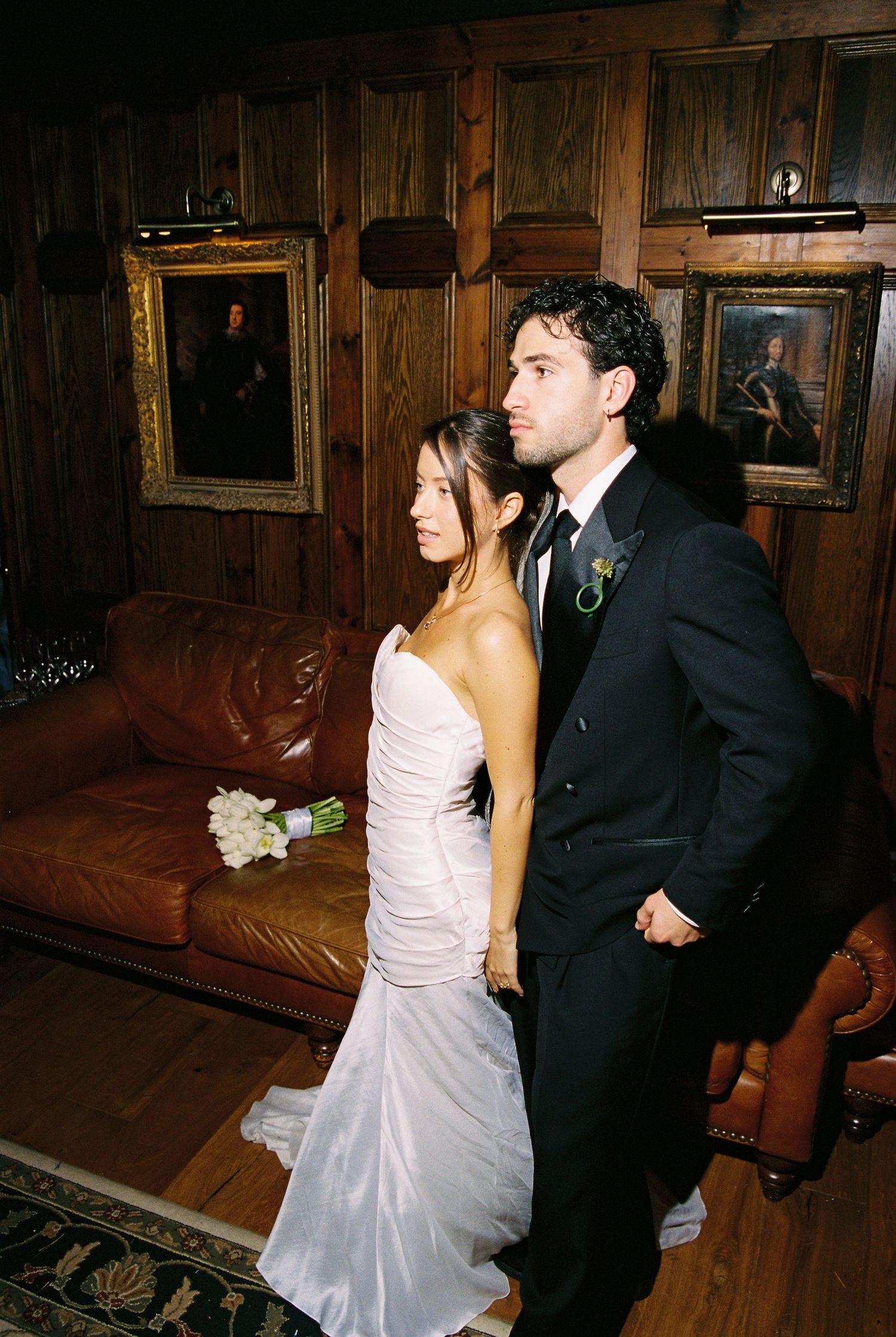 Bride in strapless white gown and groom in black suit standing in wood-paneled room.