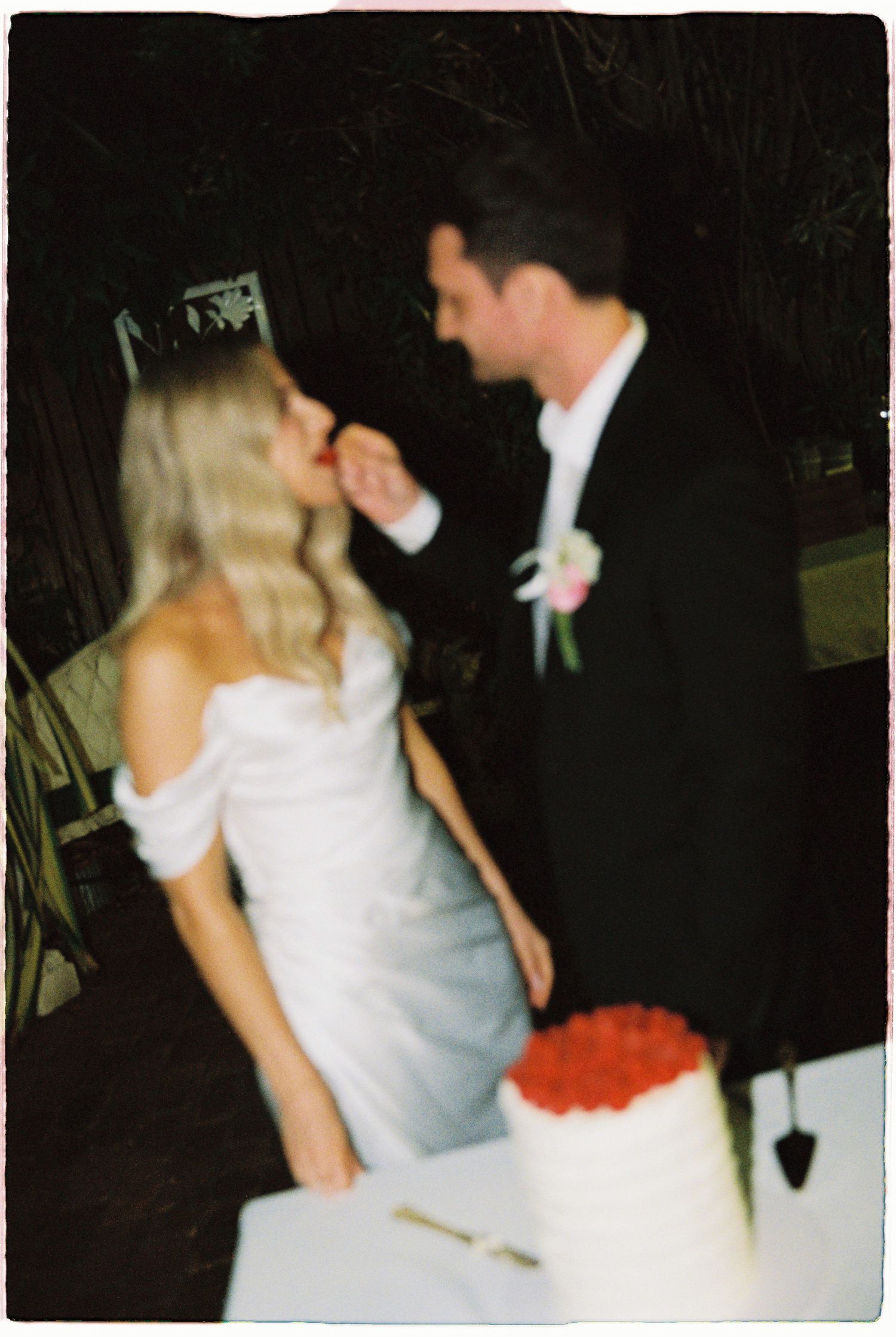Groom feeding bride a piece of wedding cake at outdoor evening reception.