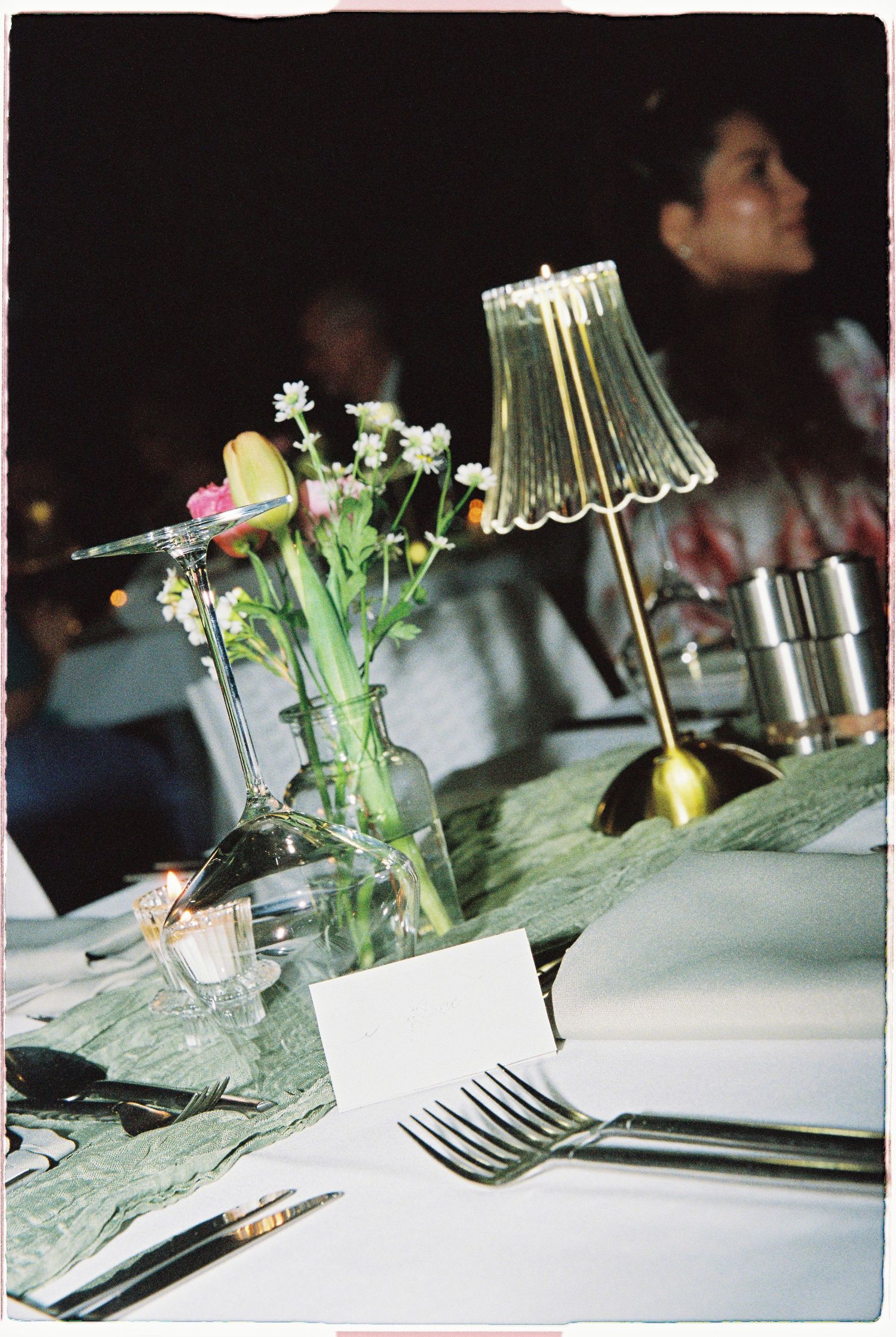 Elegant wedding table setting with small floral arrangement and gold lamp at night.