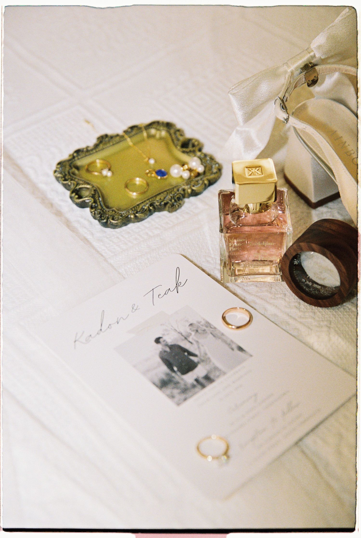 Flat lay of wedding details including rings, perfume, invitation card, and bridal shoes with bow.