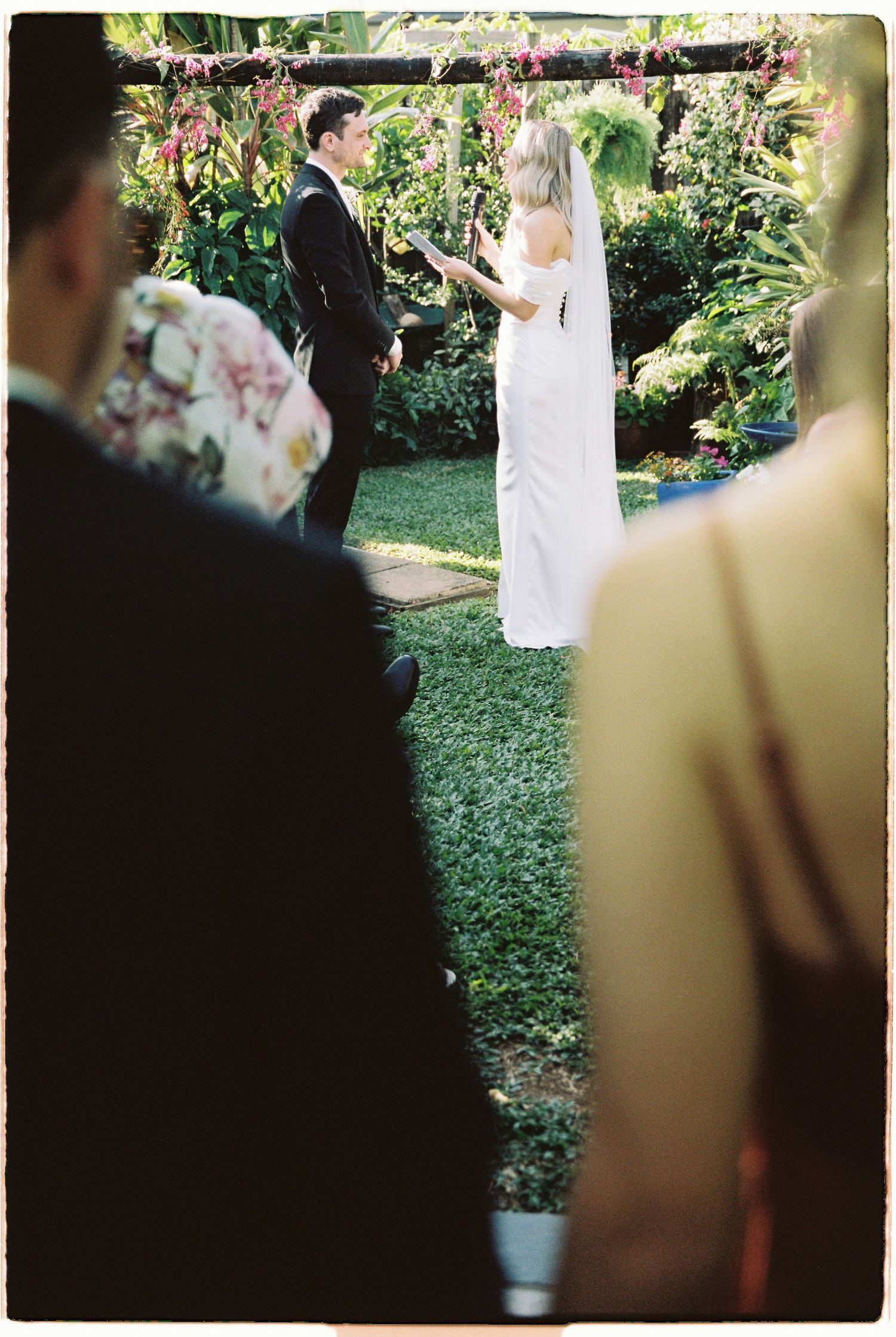 Bride and groom exchanging vows at outdoor garden wedding ceremony surrounded by tropical lush greenery.