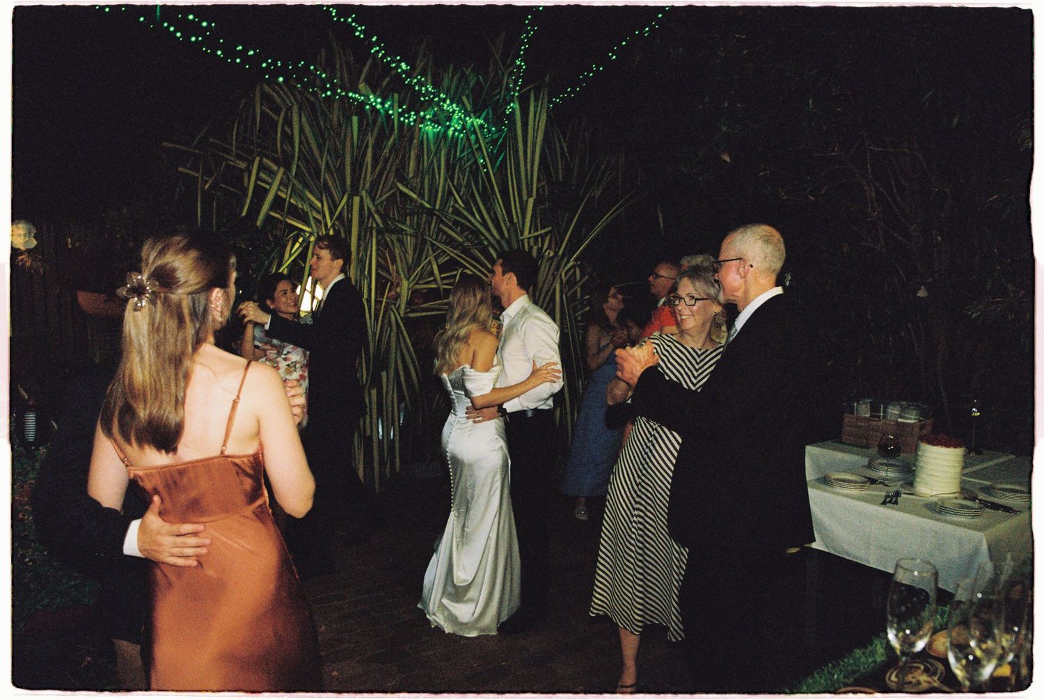 Guests dancing outdoors at night during a wedding reception surrounded by tropical greenery.