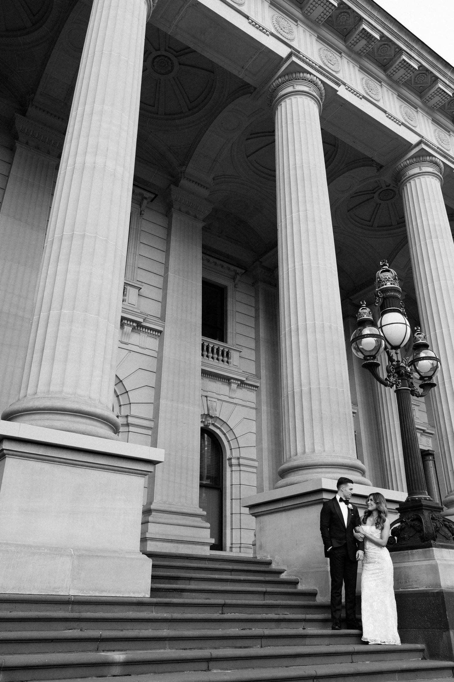 Black and white photo of newlyweds on grand steps of a classical building with tall columns.