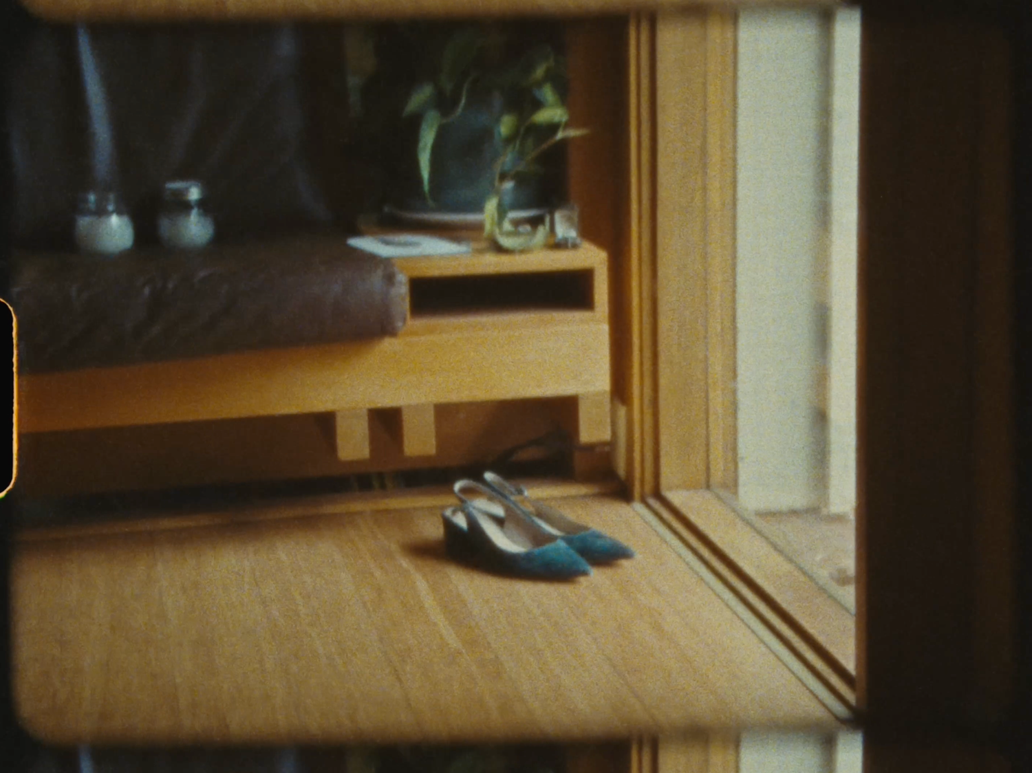 Teal blue heels placed on a wooden floor near a mid-century modern console table with a plant.