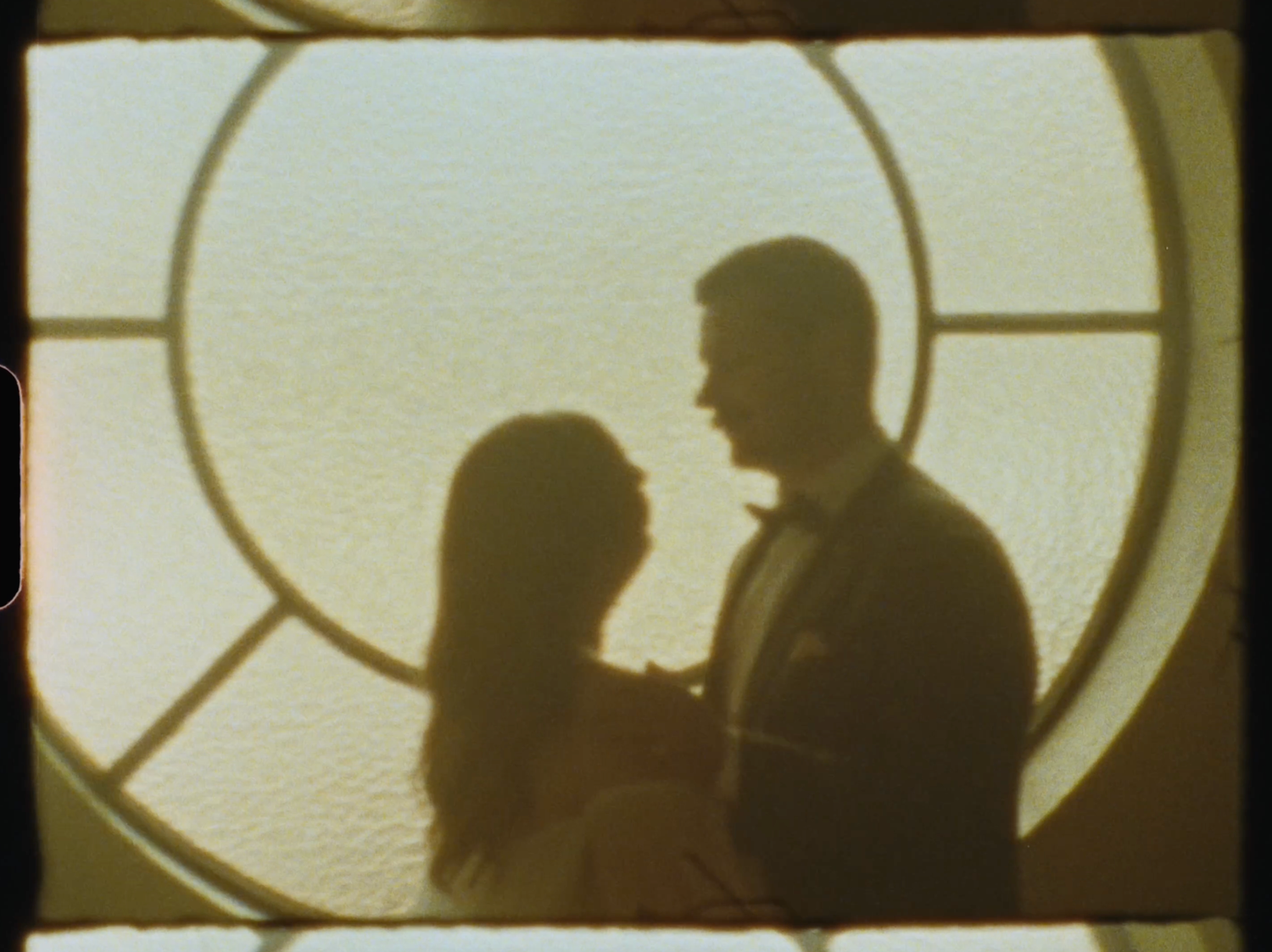 Romantic silhouette of a couple embracing in front of a circular stained glass window.