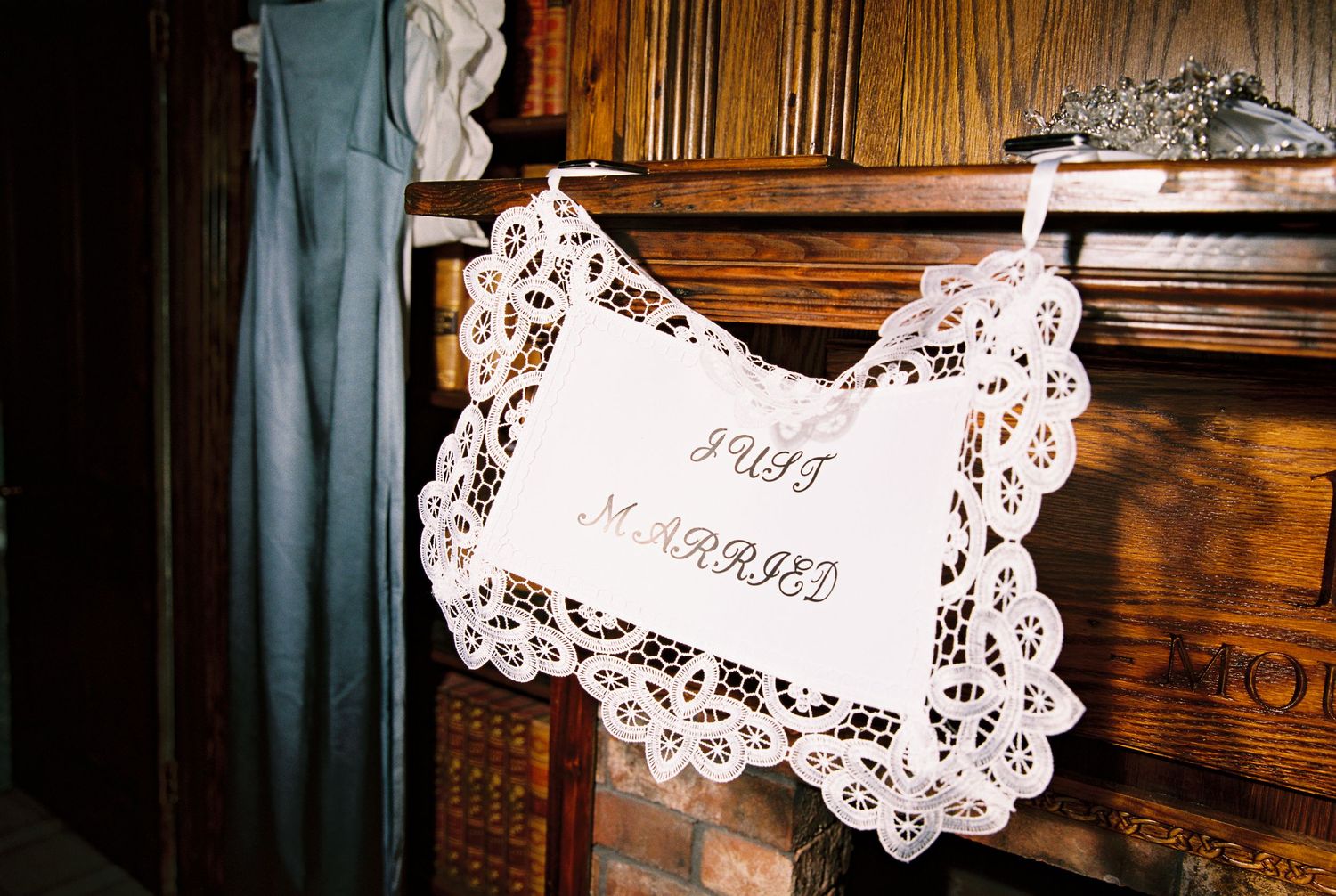 Decorative lace doily Just Married sign hanging on a rustic wooden fireplace mantel.