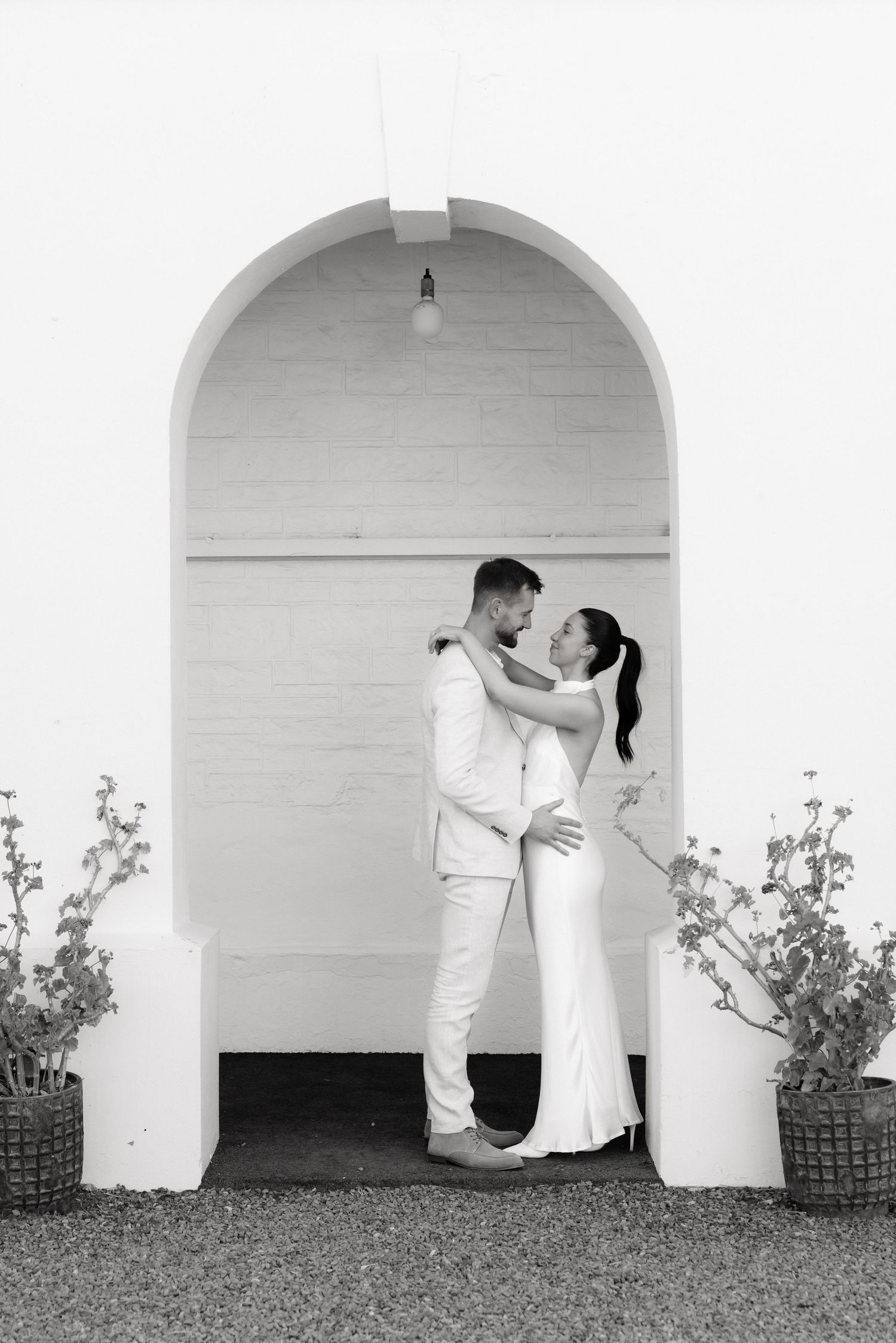 Black and white photo of a couple embracing under an arched doorway in wedding attire.